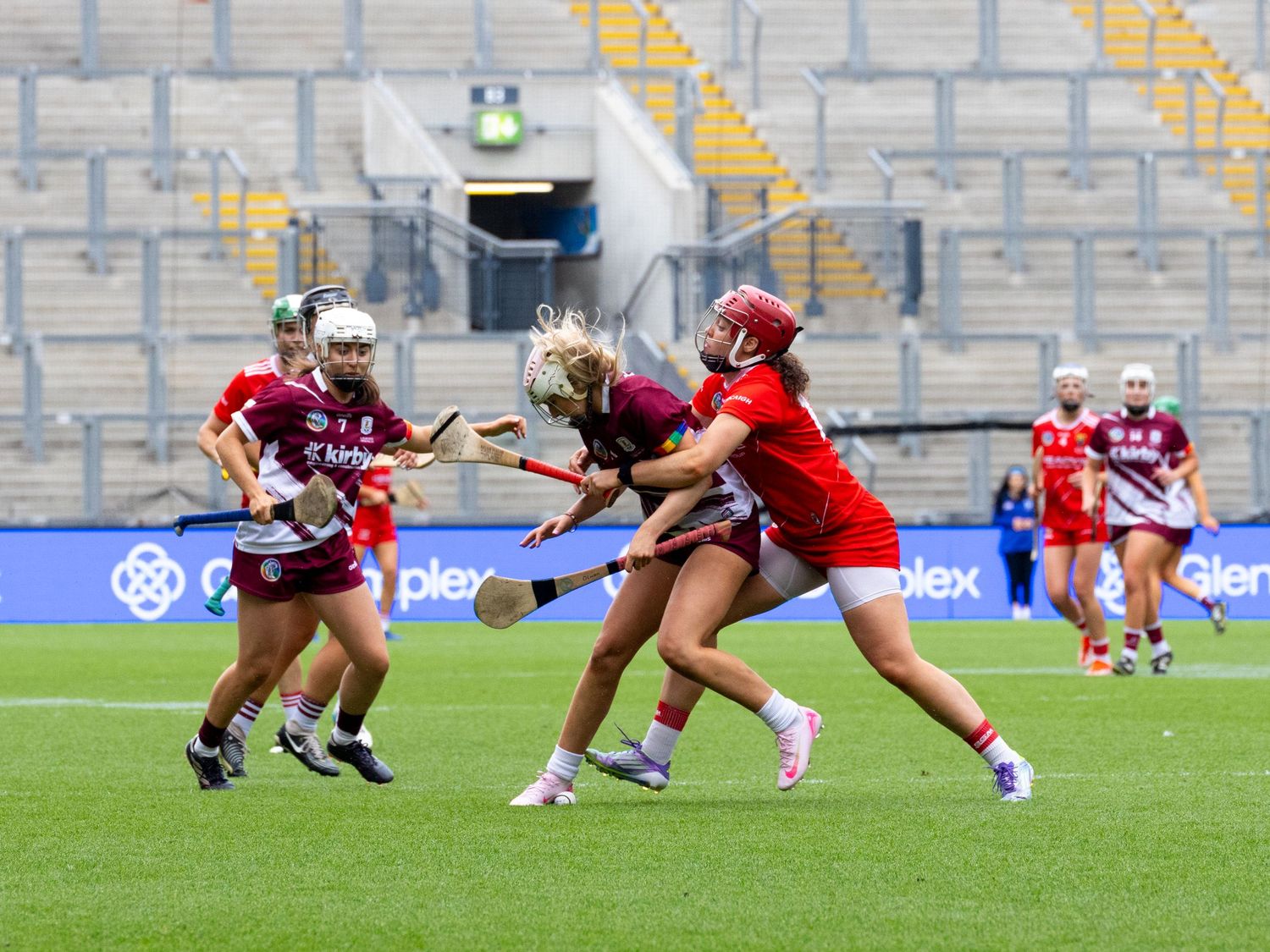 Camogie players in red and maroon jerseys battle for possession during an intense match.