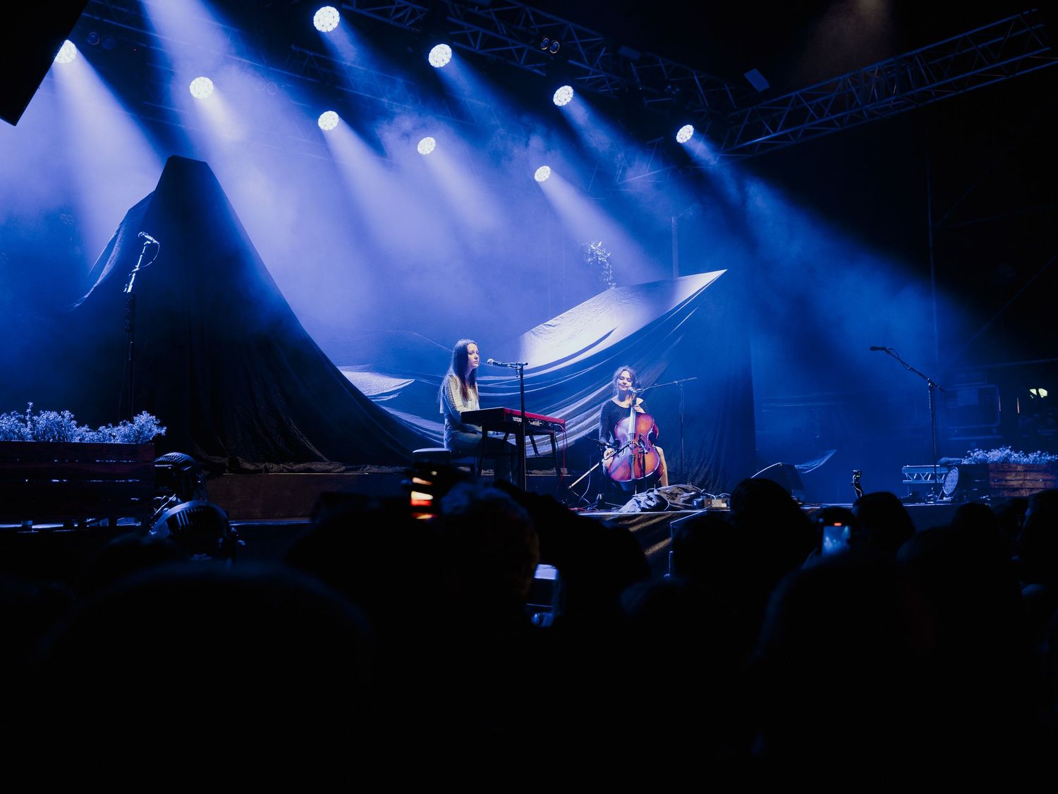 Musicians perform on stage with dramatic blue lighting and fog effects during a concert performance.