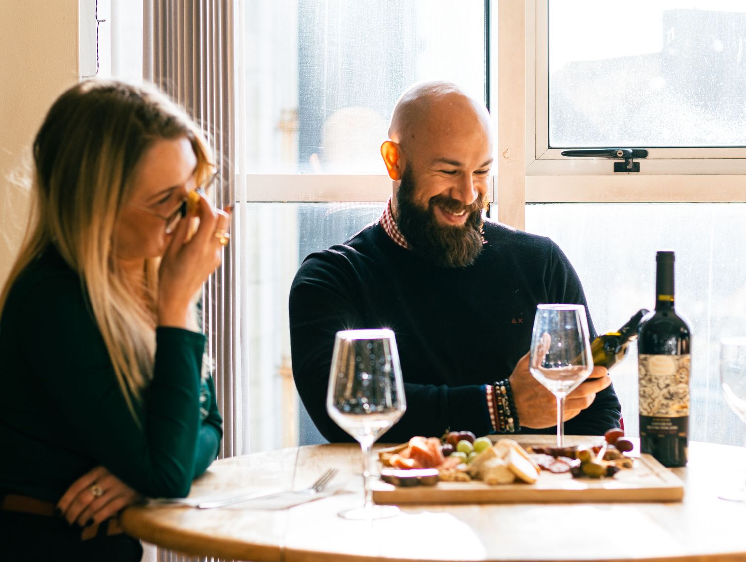 People enjoying wine and conversation at a cozy restaurant table by a window.