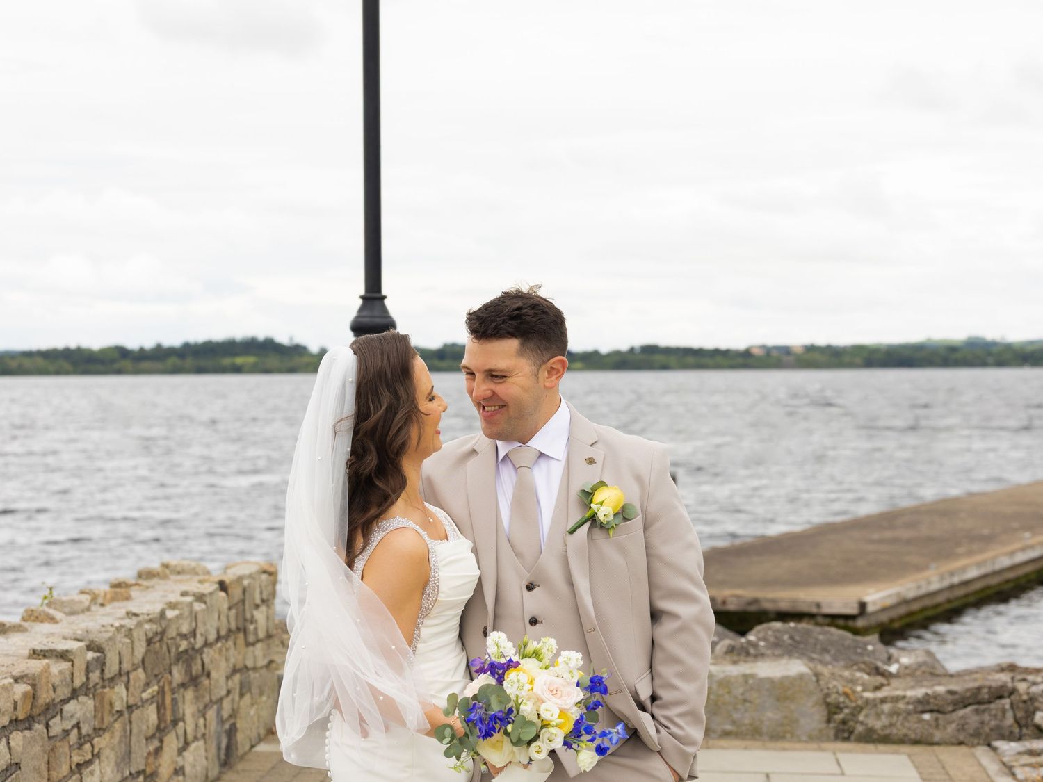 Newlyweds share romantic moments along a rocky coastal shoreline.