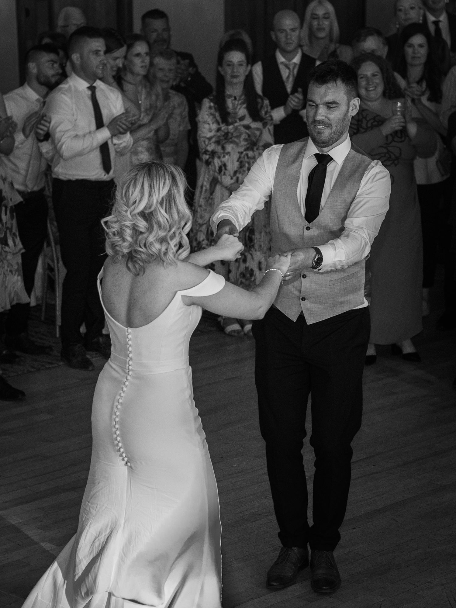 A couple dances elegantly at their wedding reception while guests look on from the sides.
