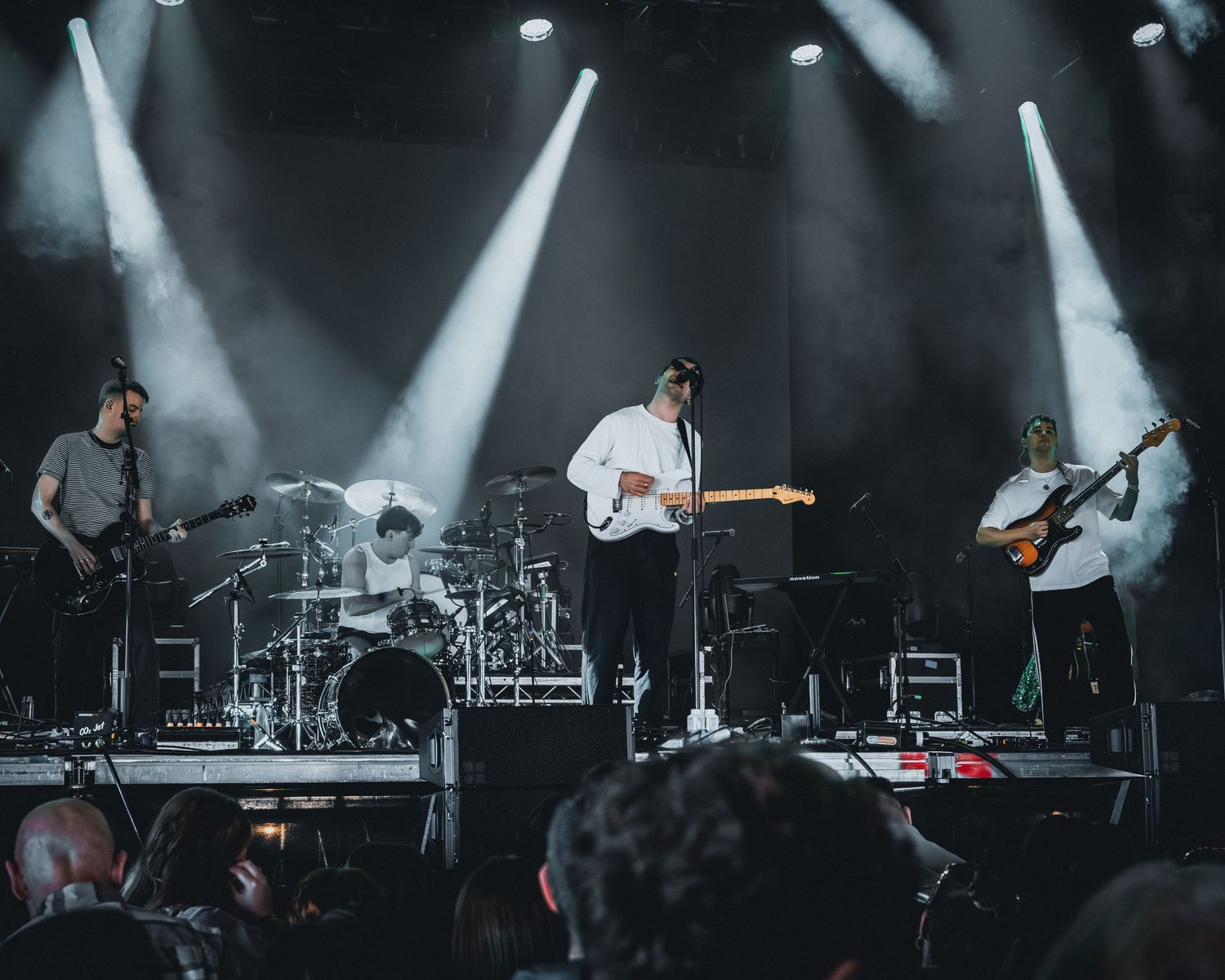 A rock band performs on a dark stage with dramatic lighting and fog effects during a live concert performance.