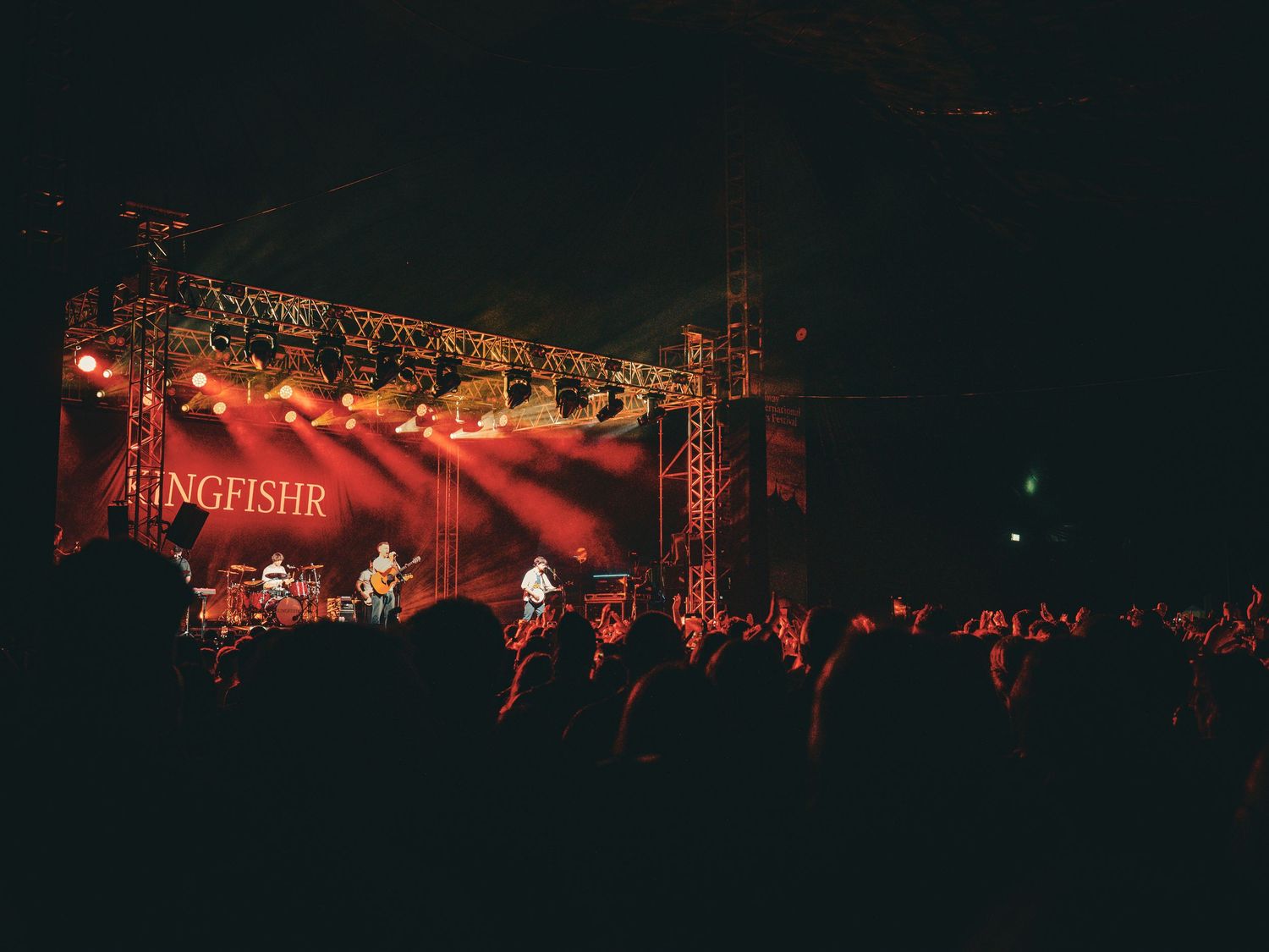 Concert stage illuminated with dramatic red lighting and smoke effects during a live performance.