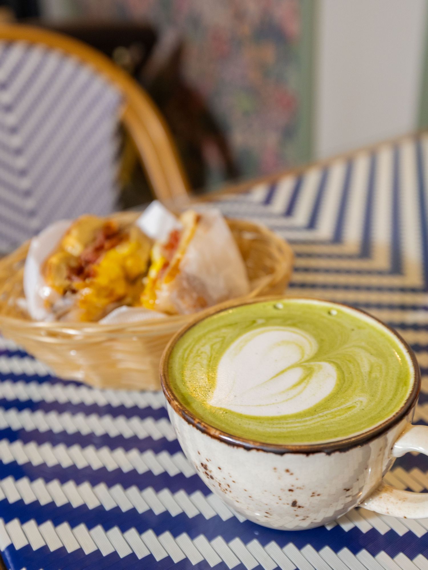 A row of green matcha lattes with white latte art served in ceramic cups on a blue and white chevron patterned surface.