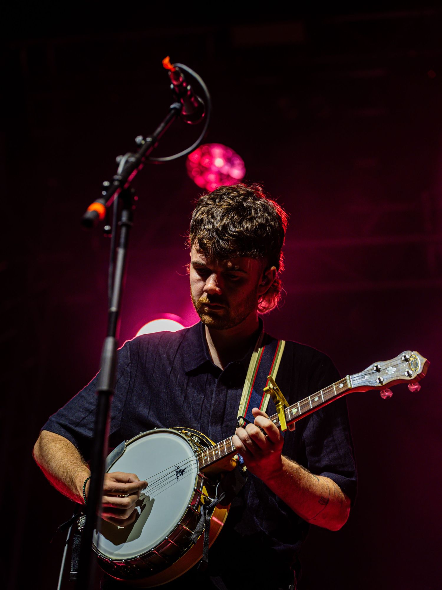 Musician plays banjo under dramatic red stage lighting during live performance.