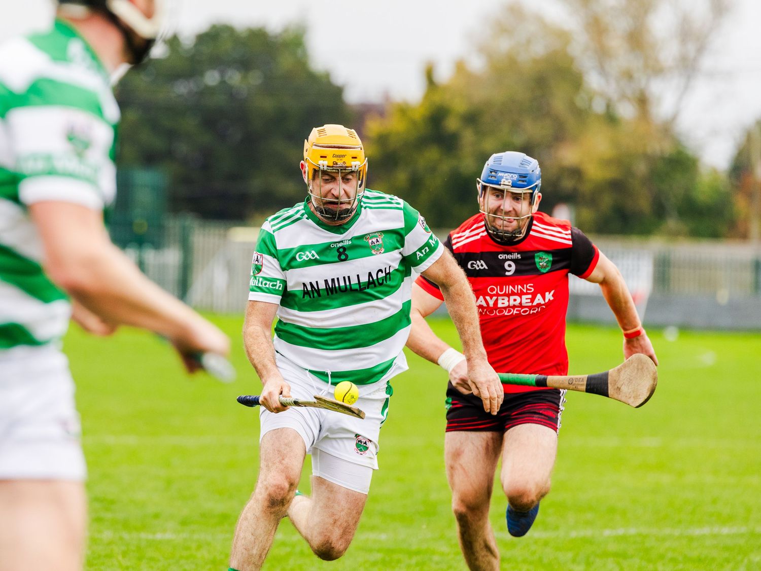 Two rugby players collide during a match between teams in green and red striped jerseys on a grass field.