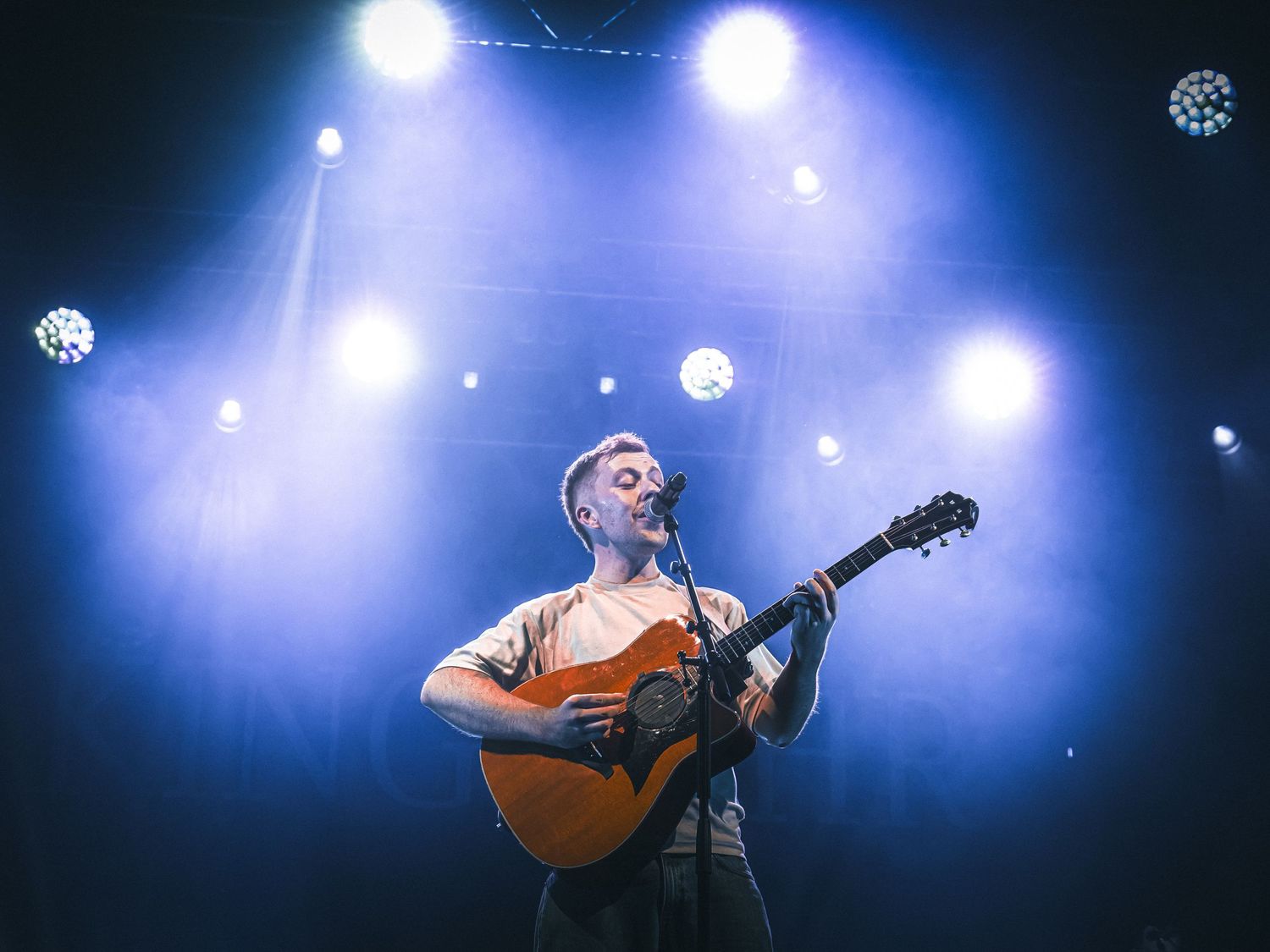 Acoustic guitarist performs under blue spotlights on concert stage.