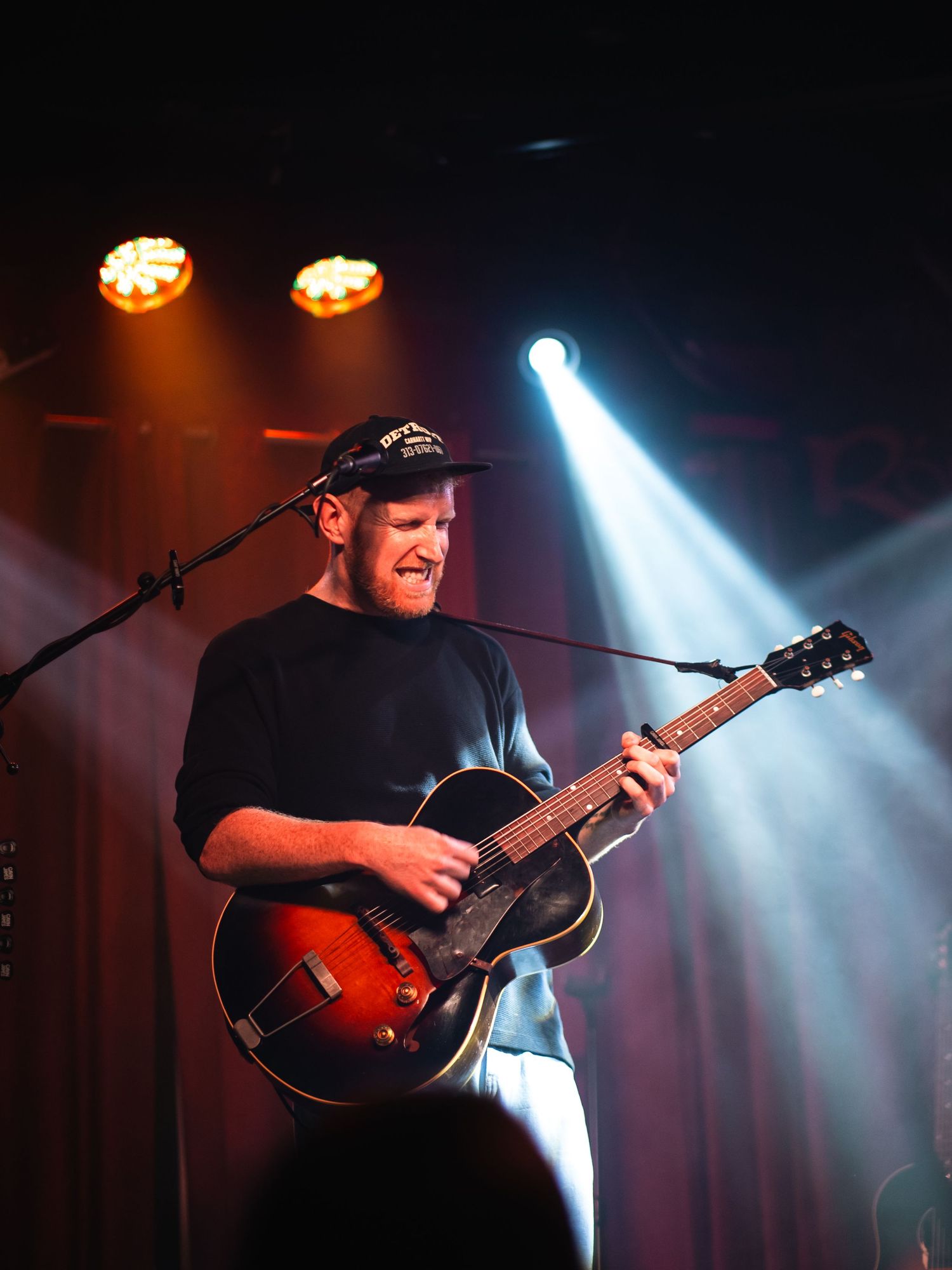Musician playing acoustic guitar under bright spotlights during a live performance.