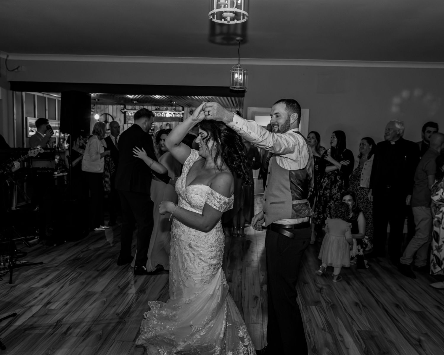Wedding guests dance together on the wooden floor at an evening reception celebration.