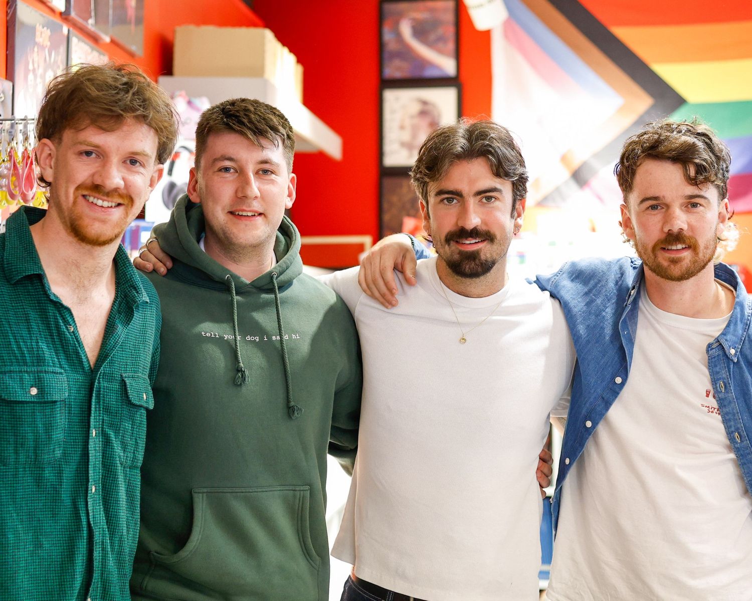 A group of people posing together in a row against a white wall with red accents.