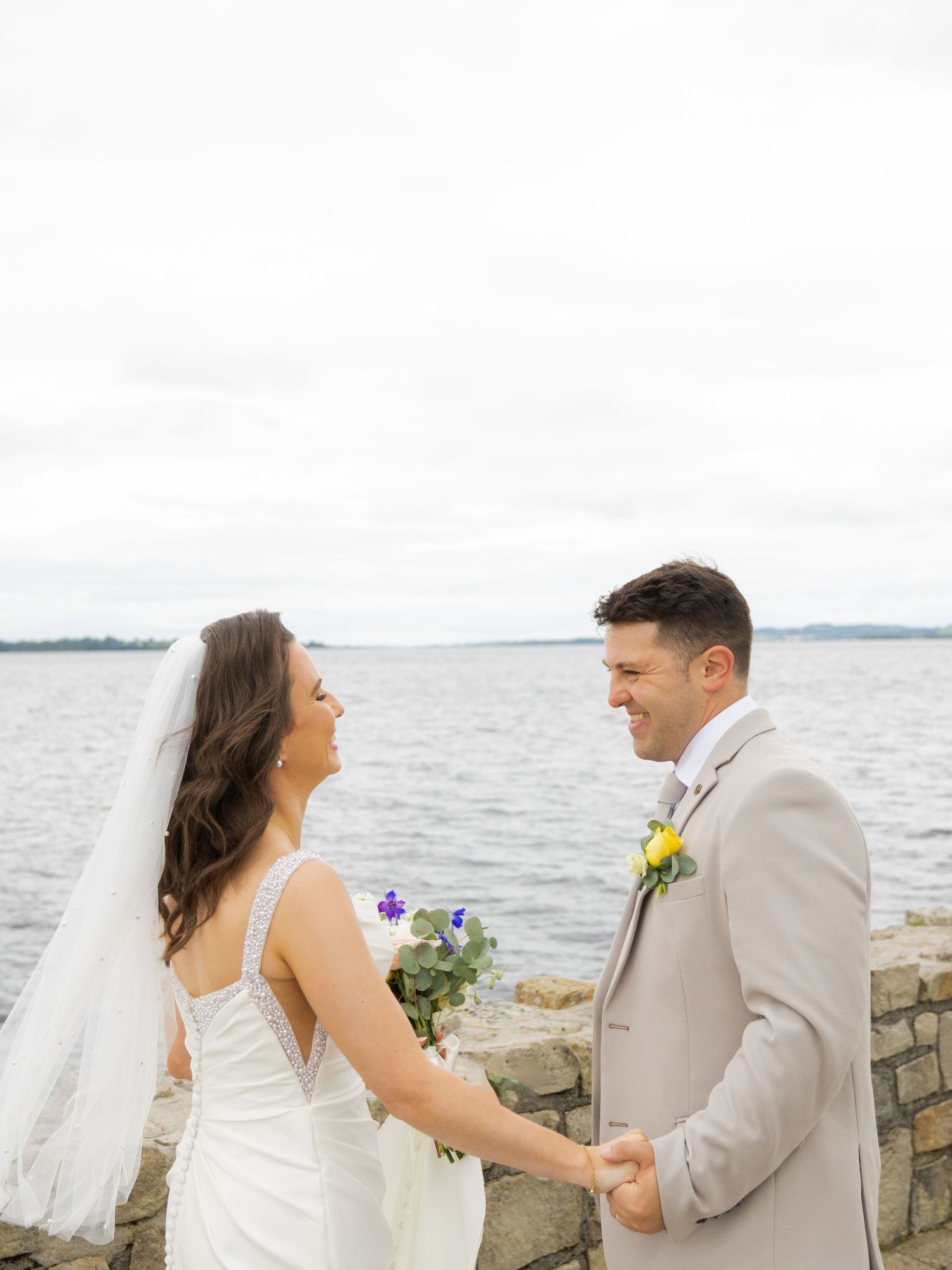 Wedding couple shares intimate moments by stone wall overlooking waterfront.