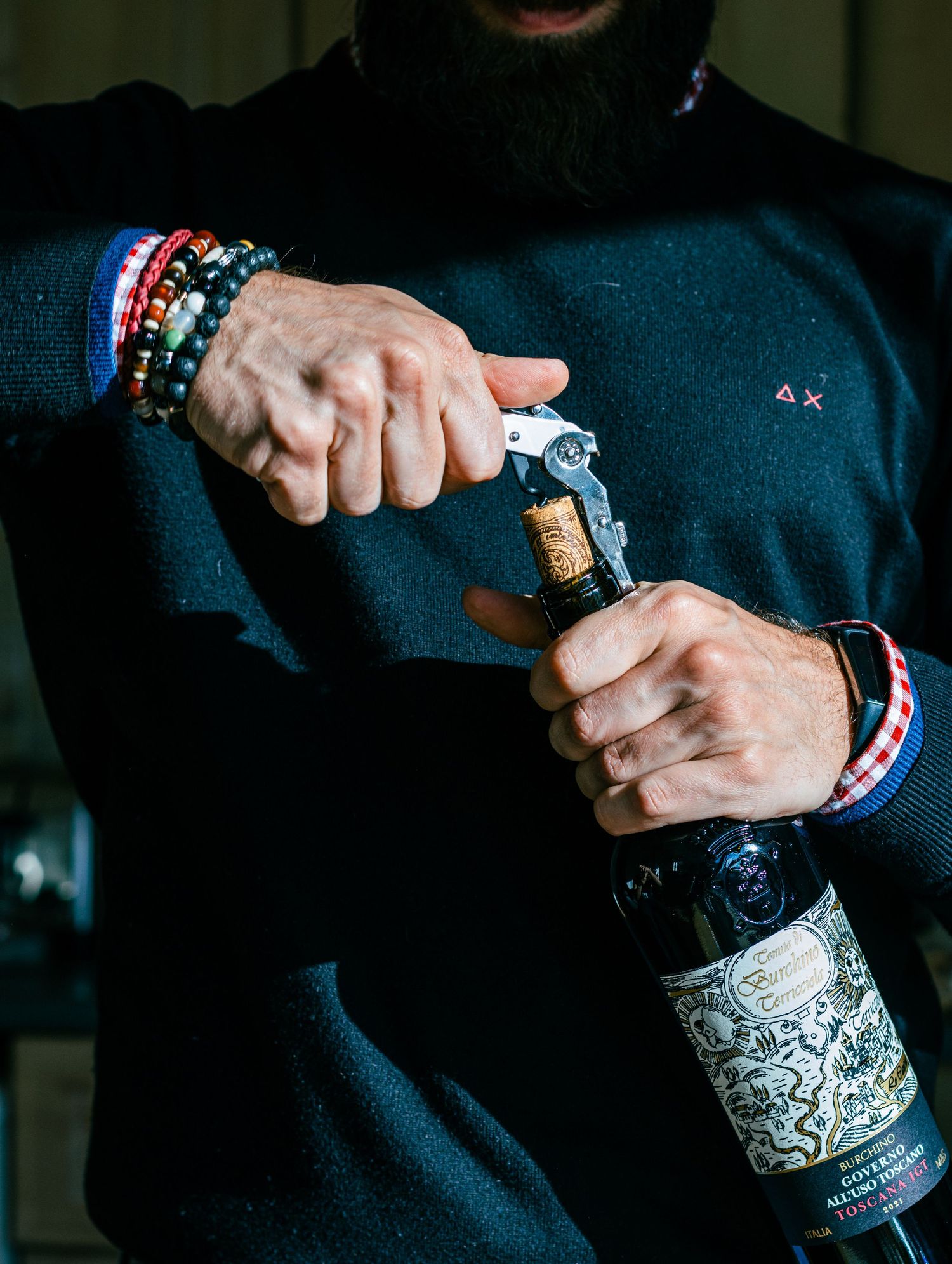 Hands holding an ornately decorated silver champagne bottle against dark background.
