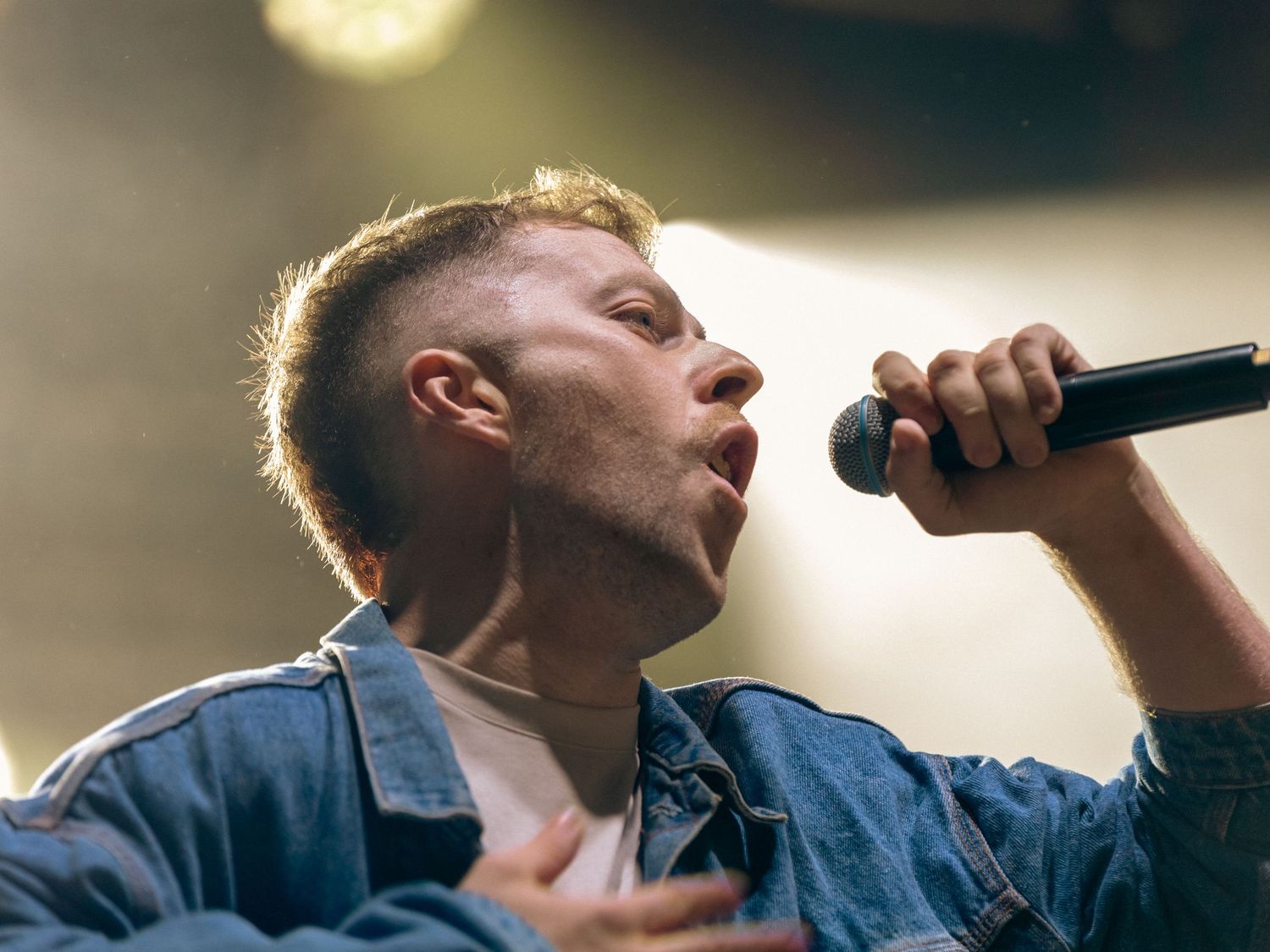 A singer performs passionately on stage with dramatic lighting and a microphone in hand.