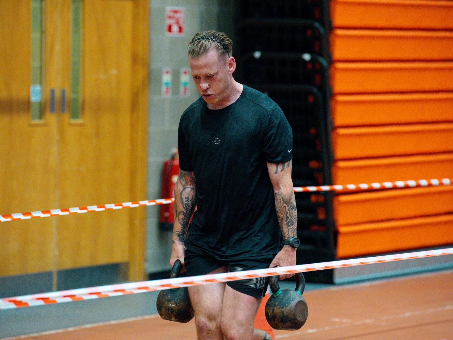 Person doing dumbbell exercises in front of orange storage lockers at a fitness facility.