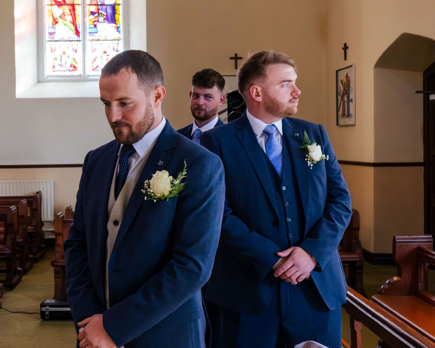Wedding party members in blue suits share smiles during a church ceremony.