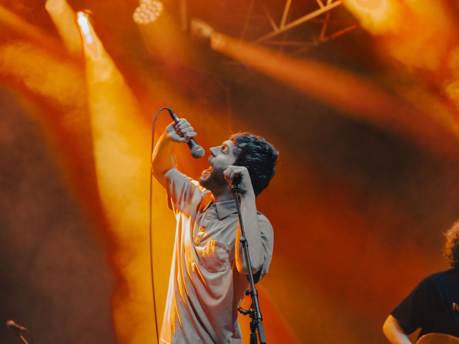 Concert performer singing passionately on stage with dramatic orange lighting and spotlights in the background.