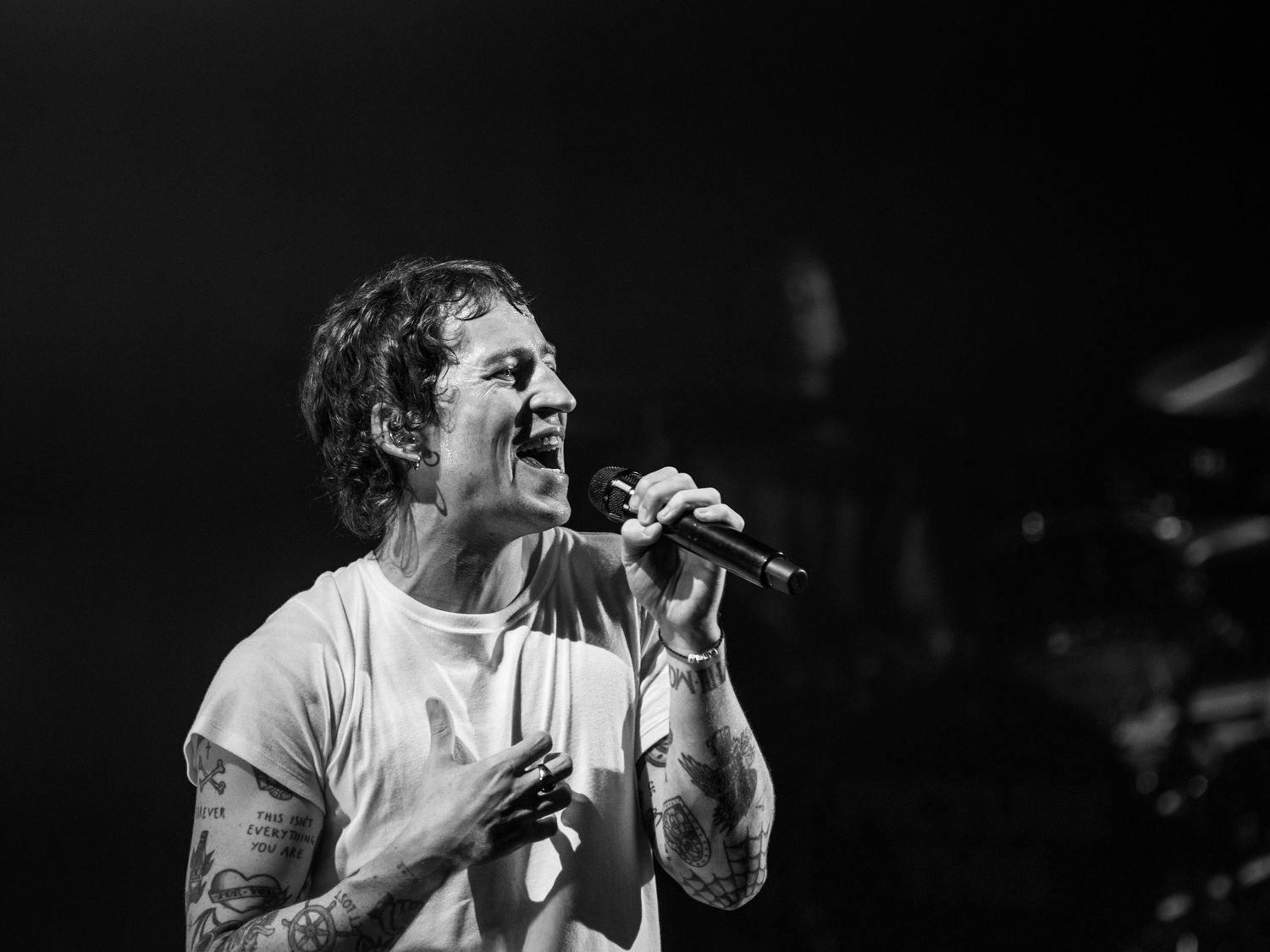Performer sings emotively in black and white stage lighting during concert.