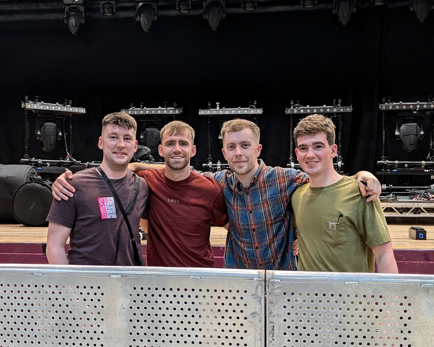 Four people stand together smiling in front of a perforated metal wall.