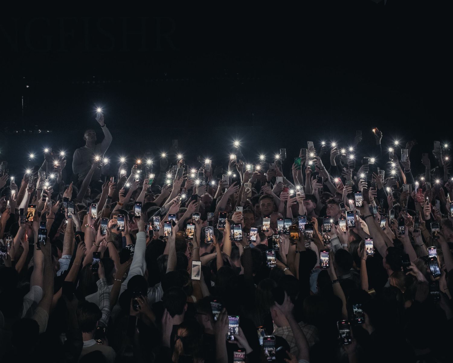 Concert crowd holds up illuminated phones during nighttime performance creating a sea of lights.