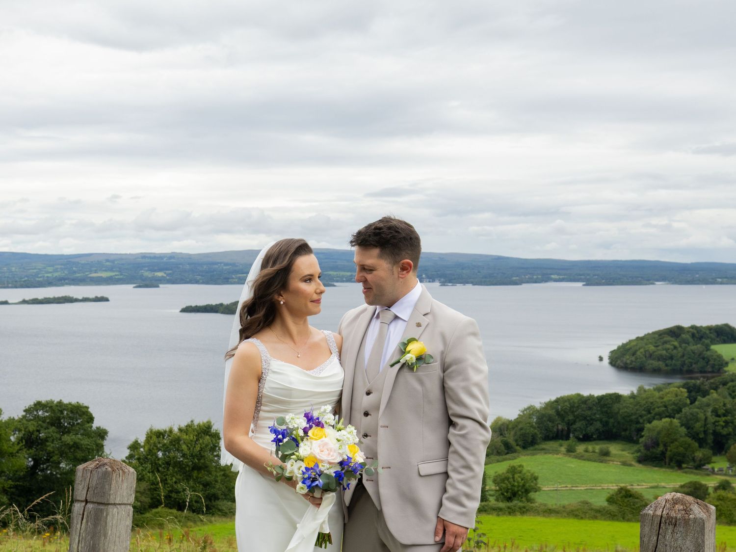 Couple in wedding attire share an intimate moment overlooking a scenic lake and mountain landscape.