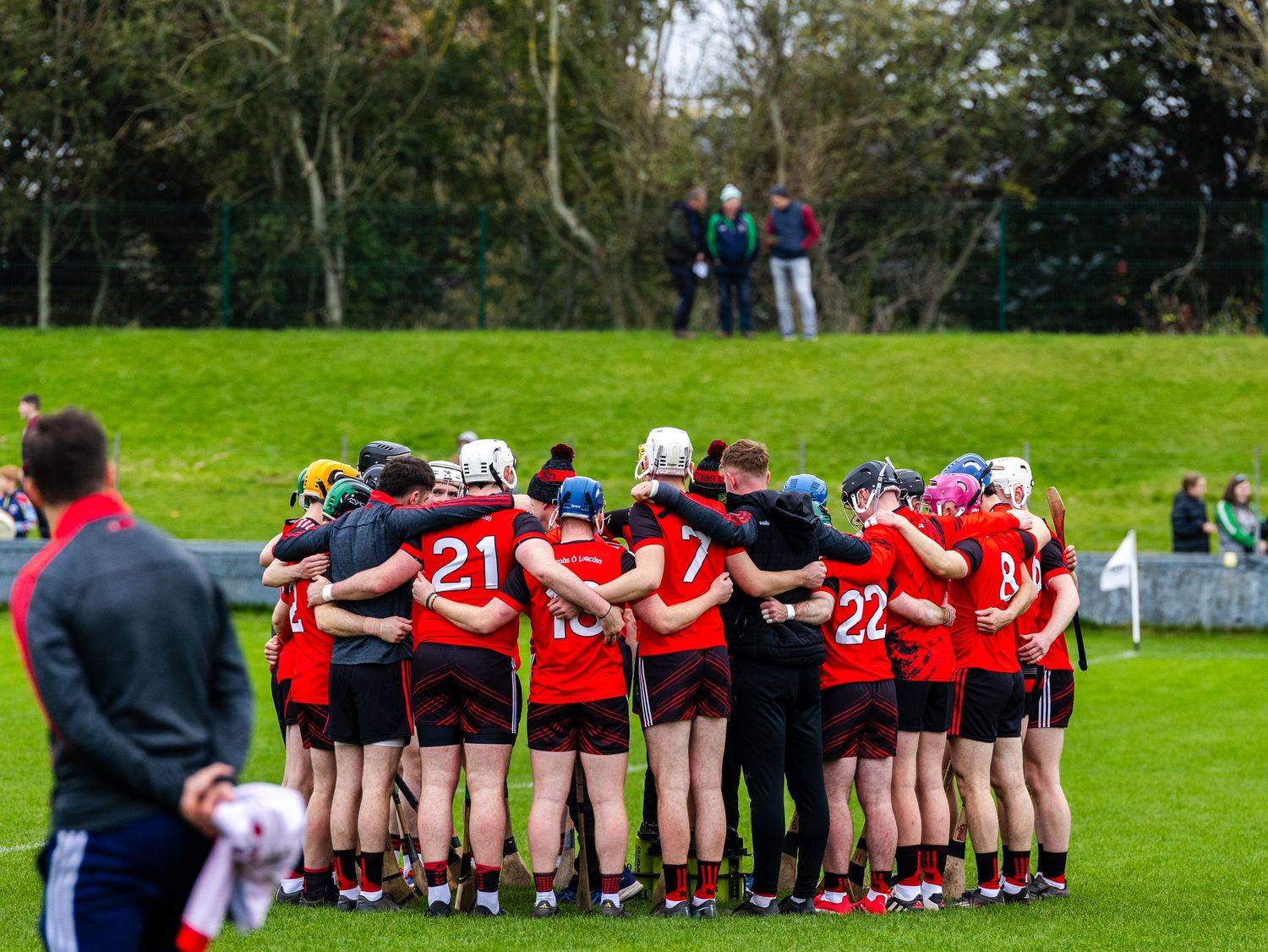 Rugby players huddle together in a line formation on a green grass field during a match or practice session.