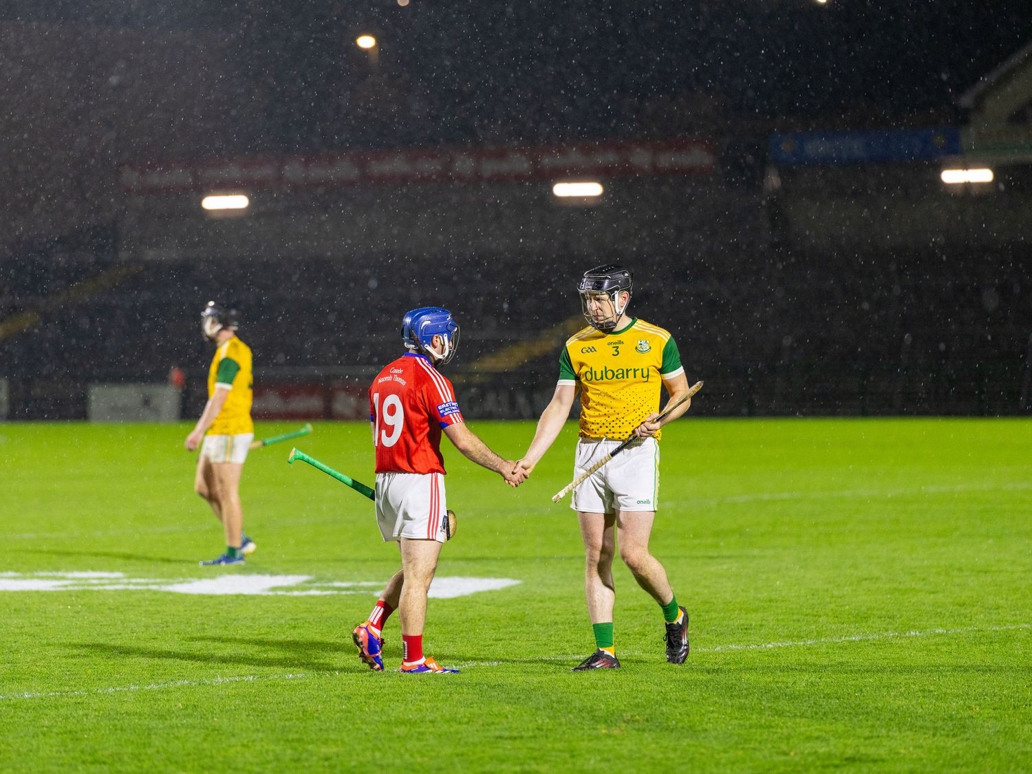 A series of athletes playing Gaelic football on a grass field at night under stadium lights.