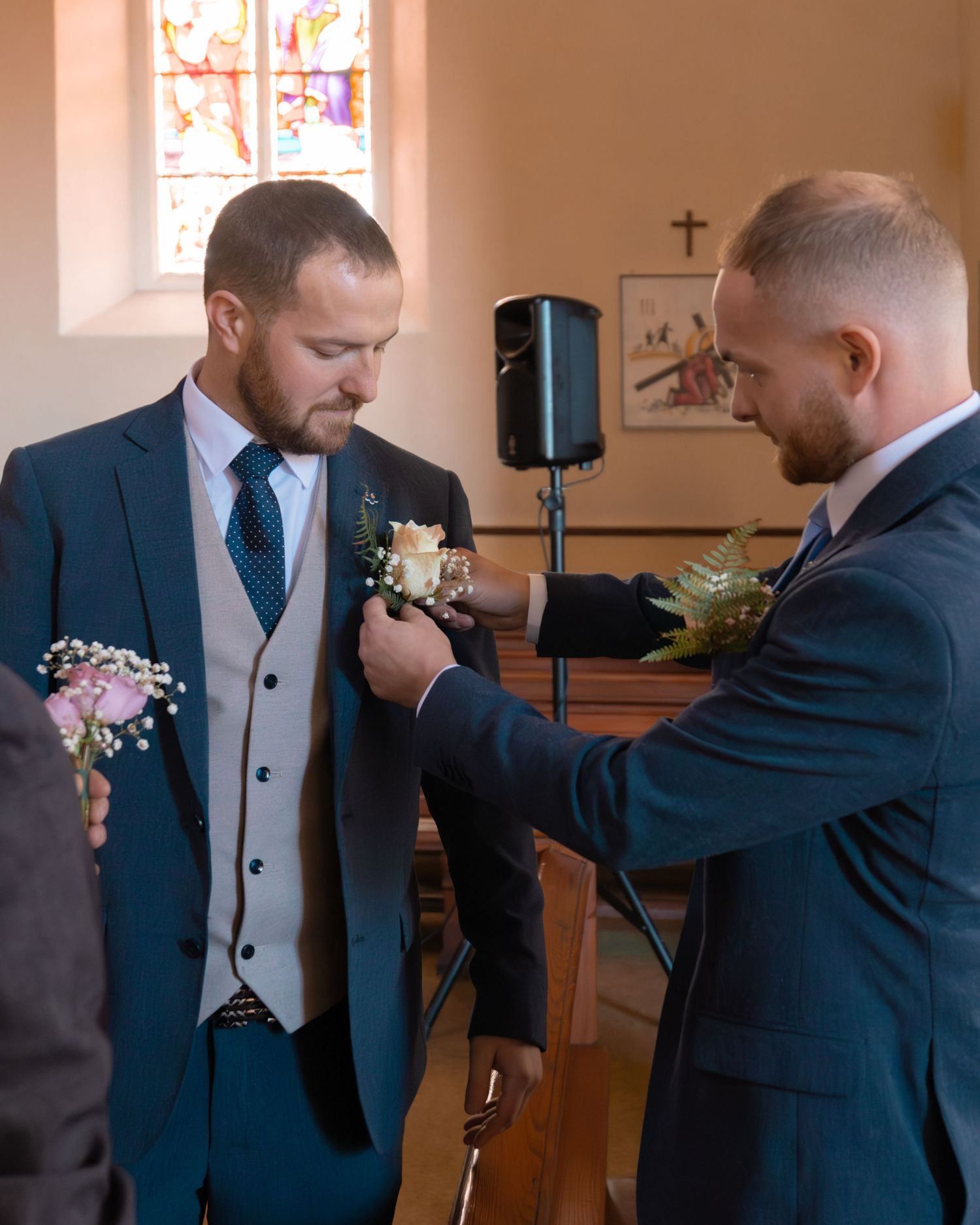 Groomsmen helping each other pin boutonnieres in a church room before the ceremony.
