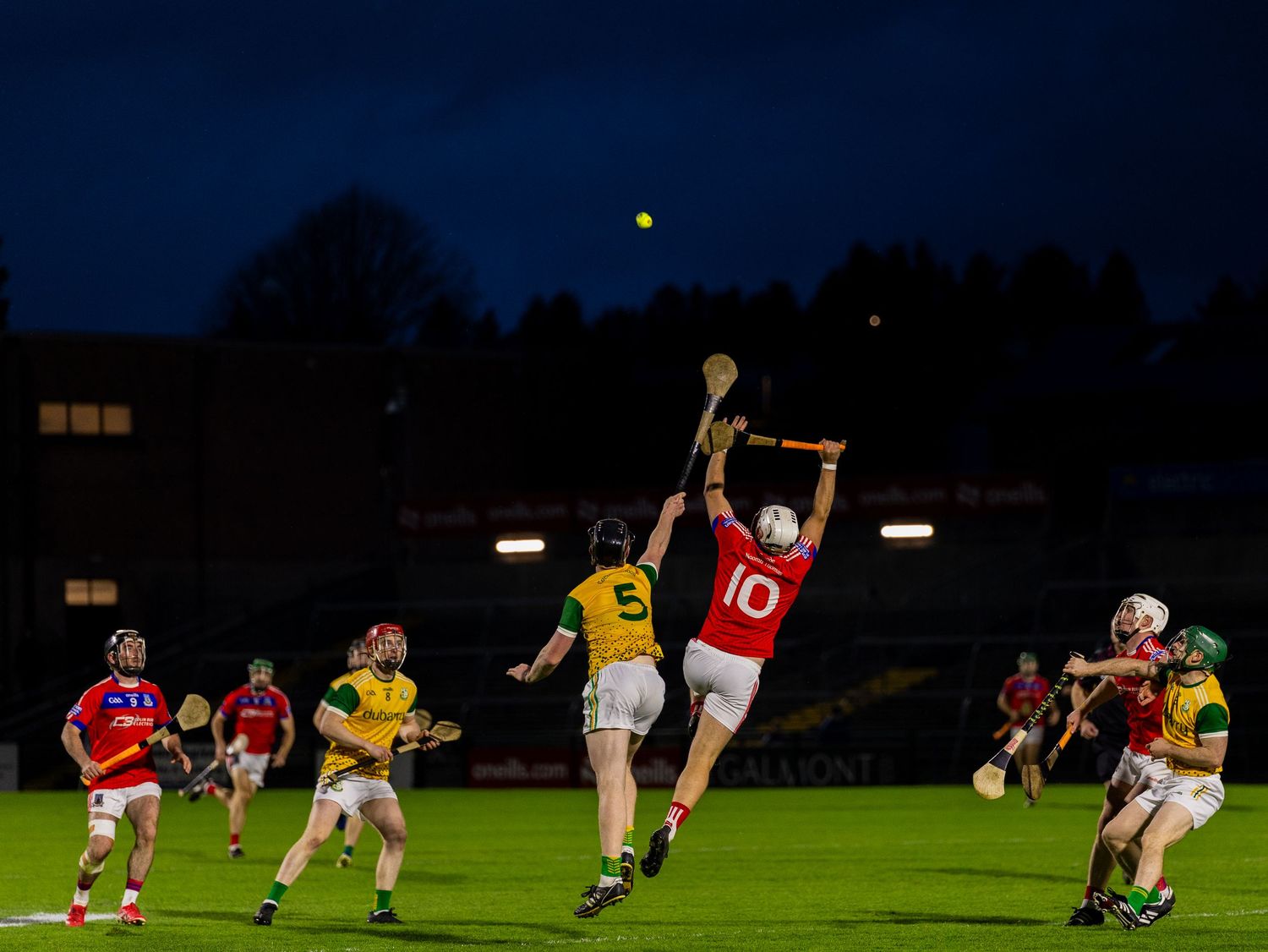 Rugby players compete for possession during a nighttime match under bright stadium lights.