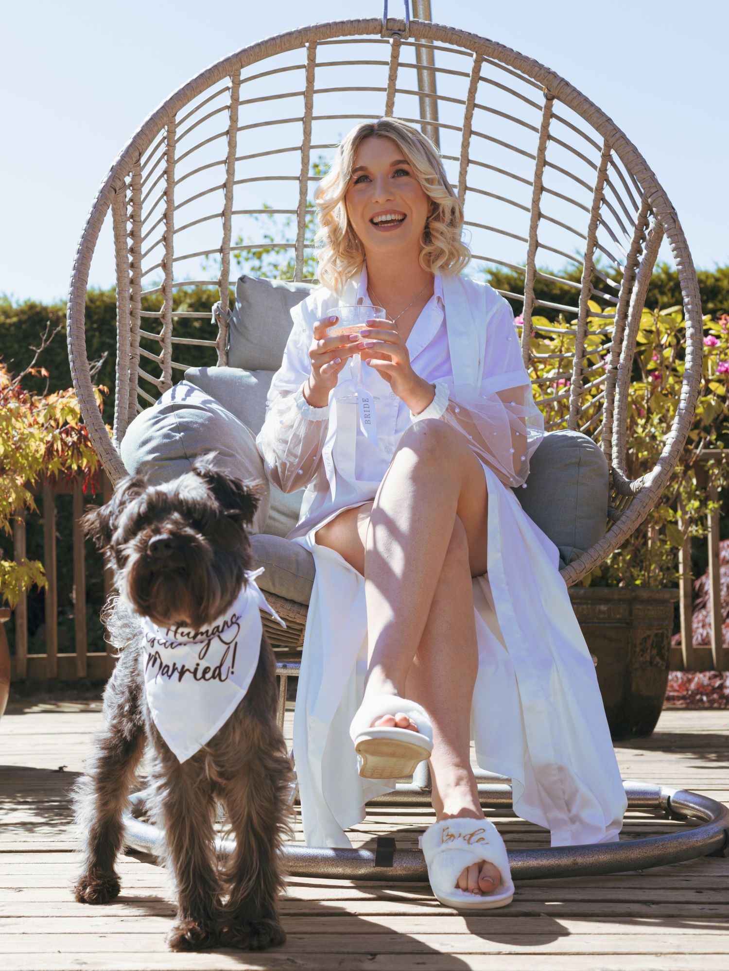 Person in white relaxing on an outdoor swing with a small dog on a sunny patio.