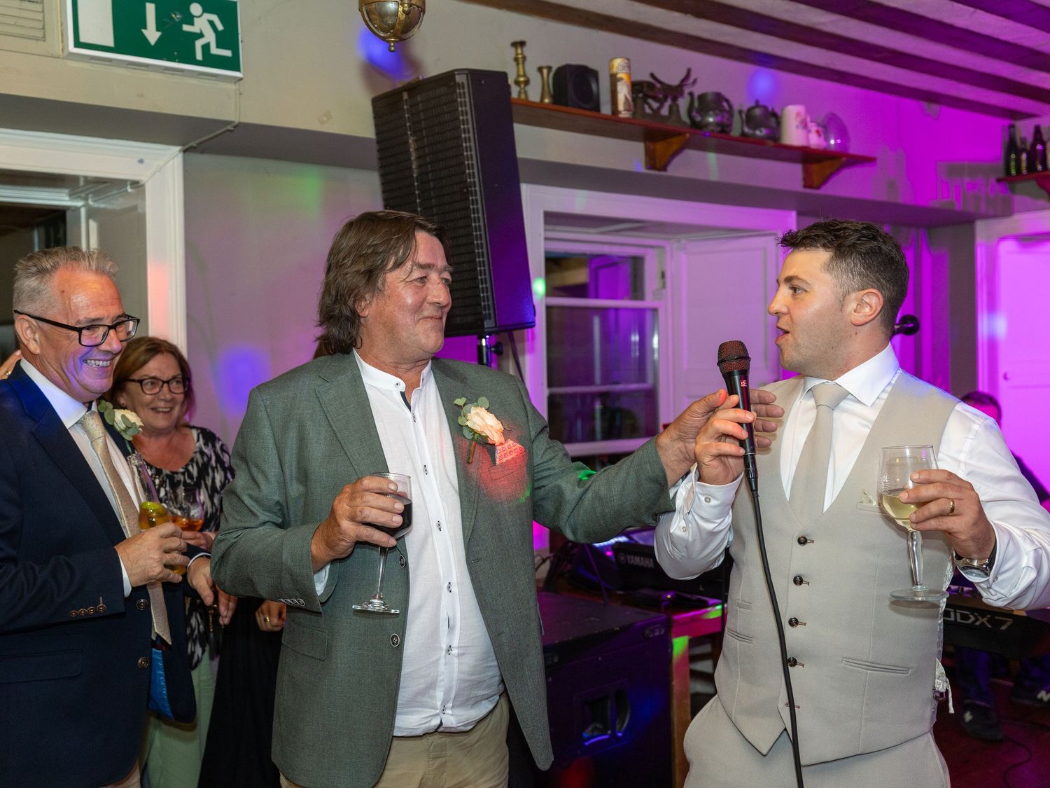 Wedding guests toasting with drinks under purple venue lighting.
