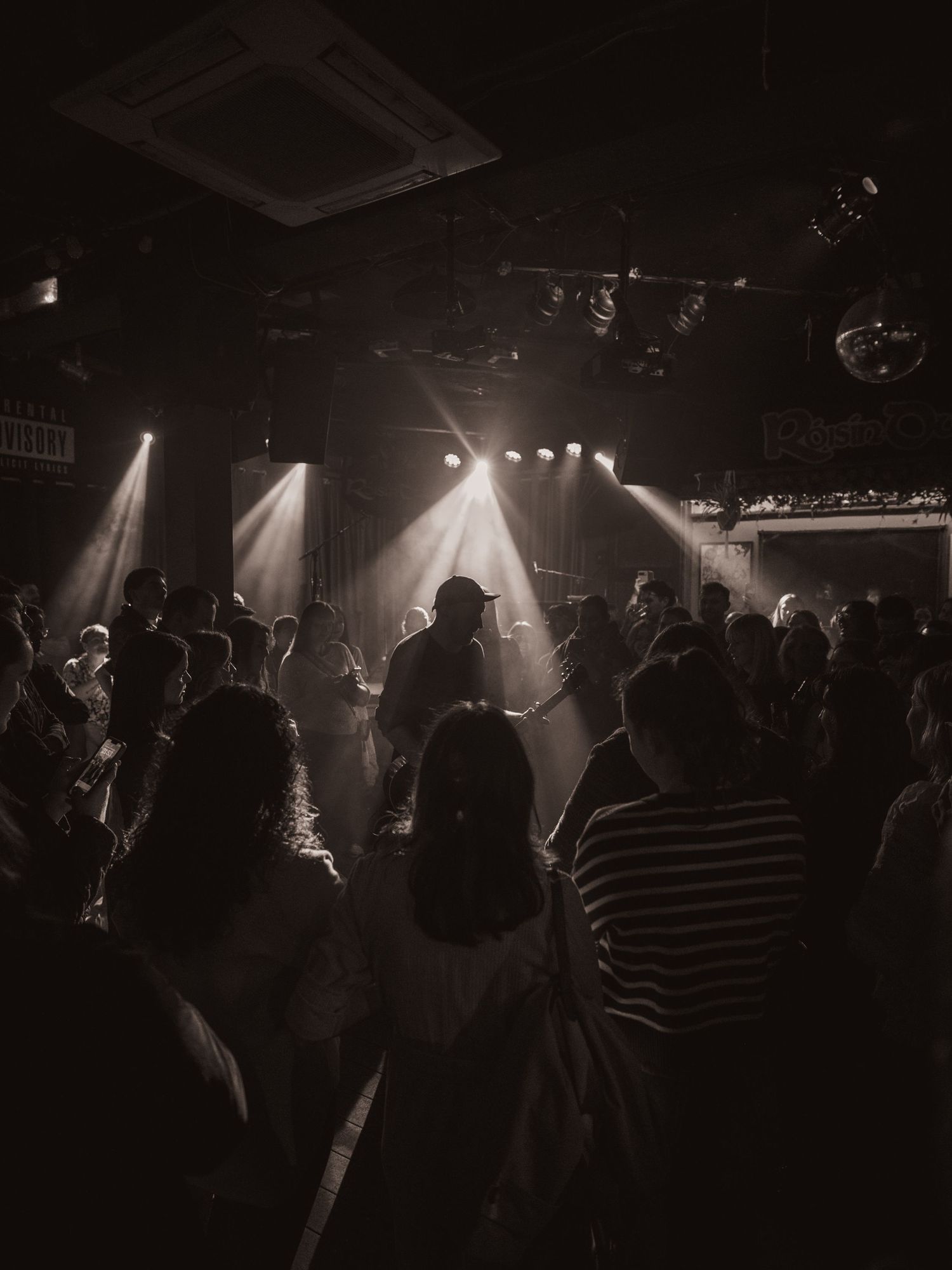 Silhouetted crowd at a concert venue with dramatic stage lighting creating an atmospheric scene.