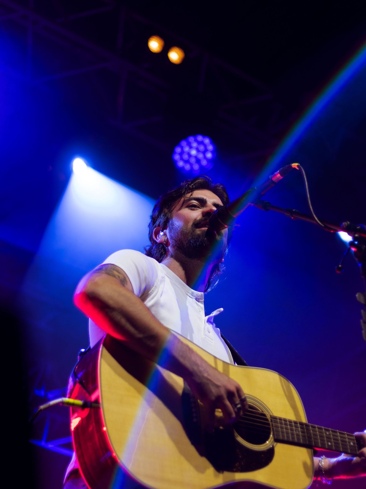 A musician performs on stage with an acoustic guitar under dramatic blue stage lighting.