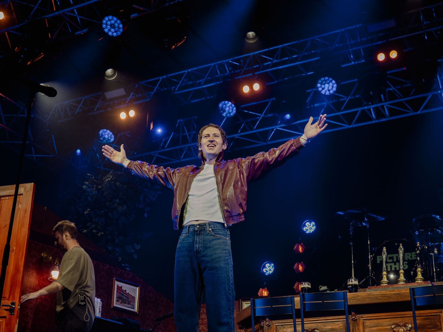 Concert performers on stage with dramatic blue lighting and stage equipment visible in background.