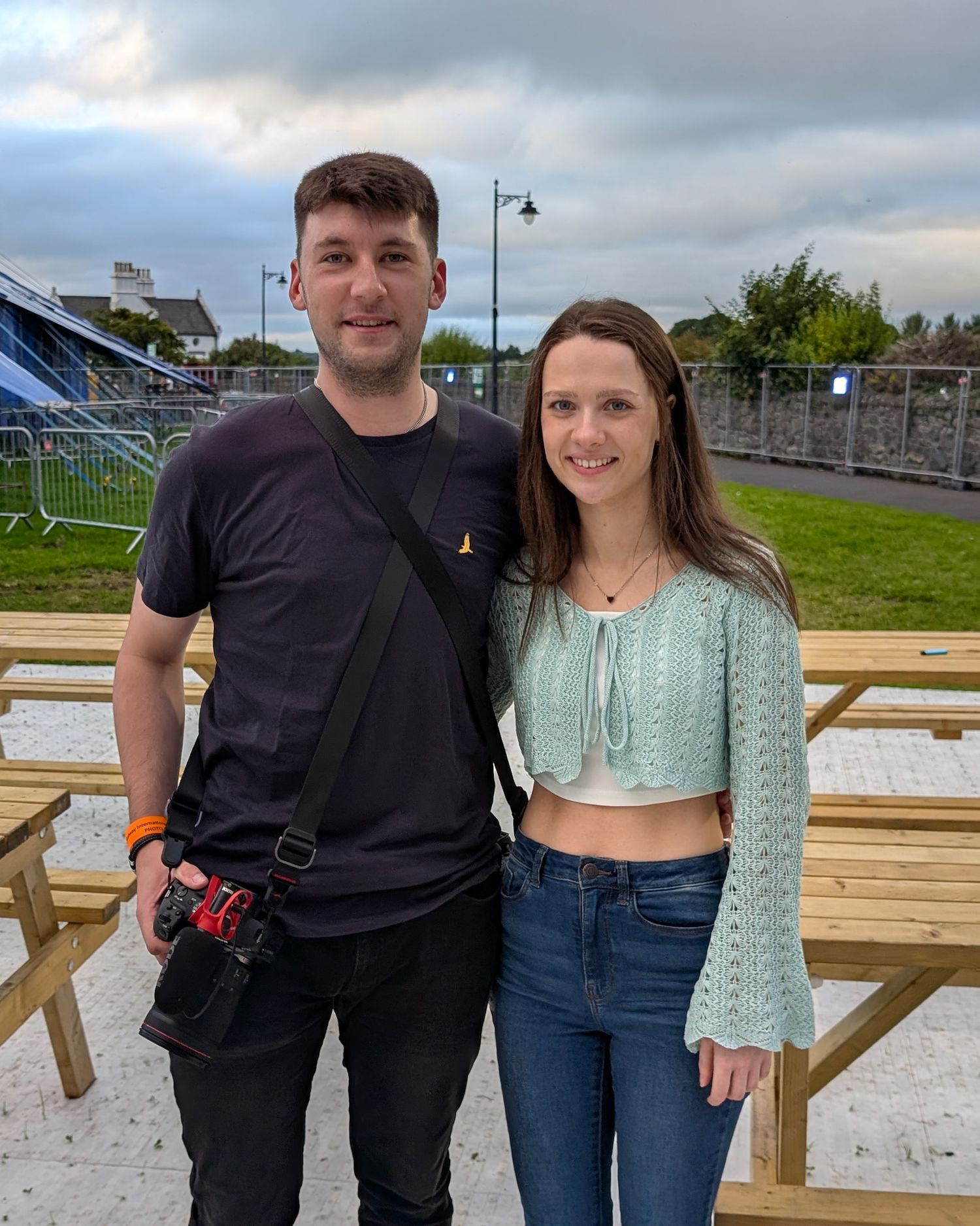 Two people standing together on a wooden deck with cloudy skies in the background.