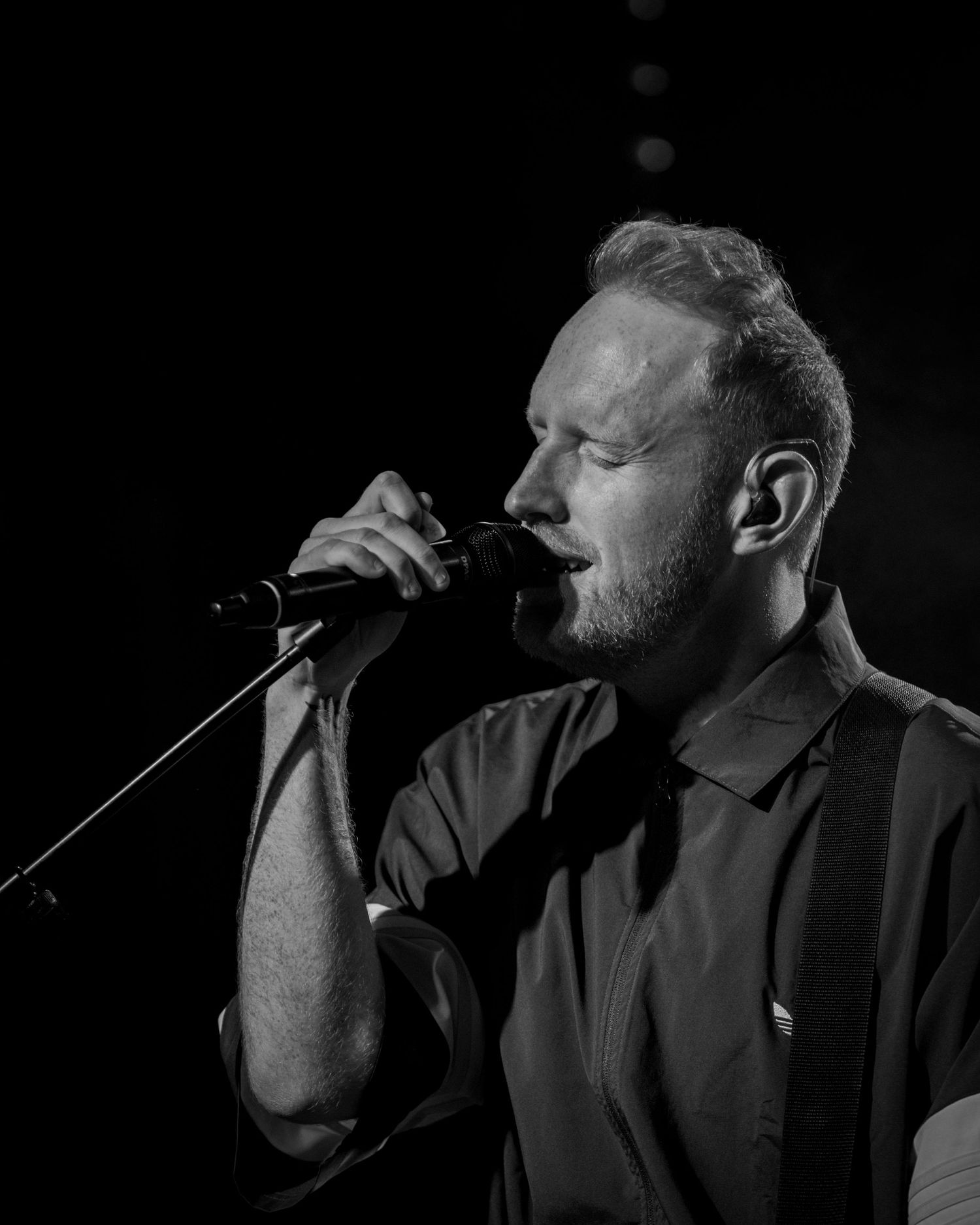 Dark moody profile shot of performer singing on stage with dramatic lighting.