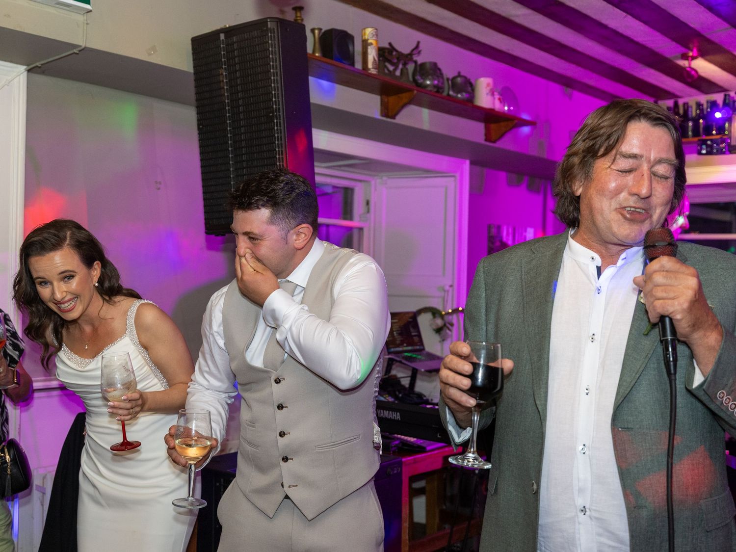 Wedding reception celebration with purple lighting and guests raising glasses.
