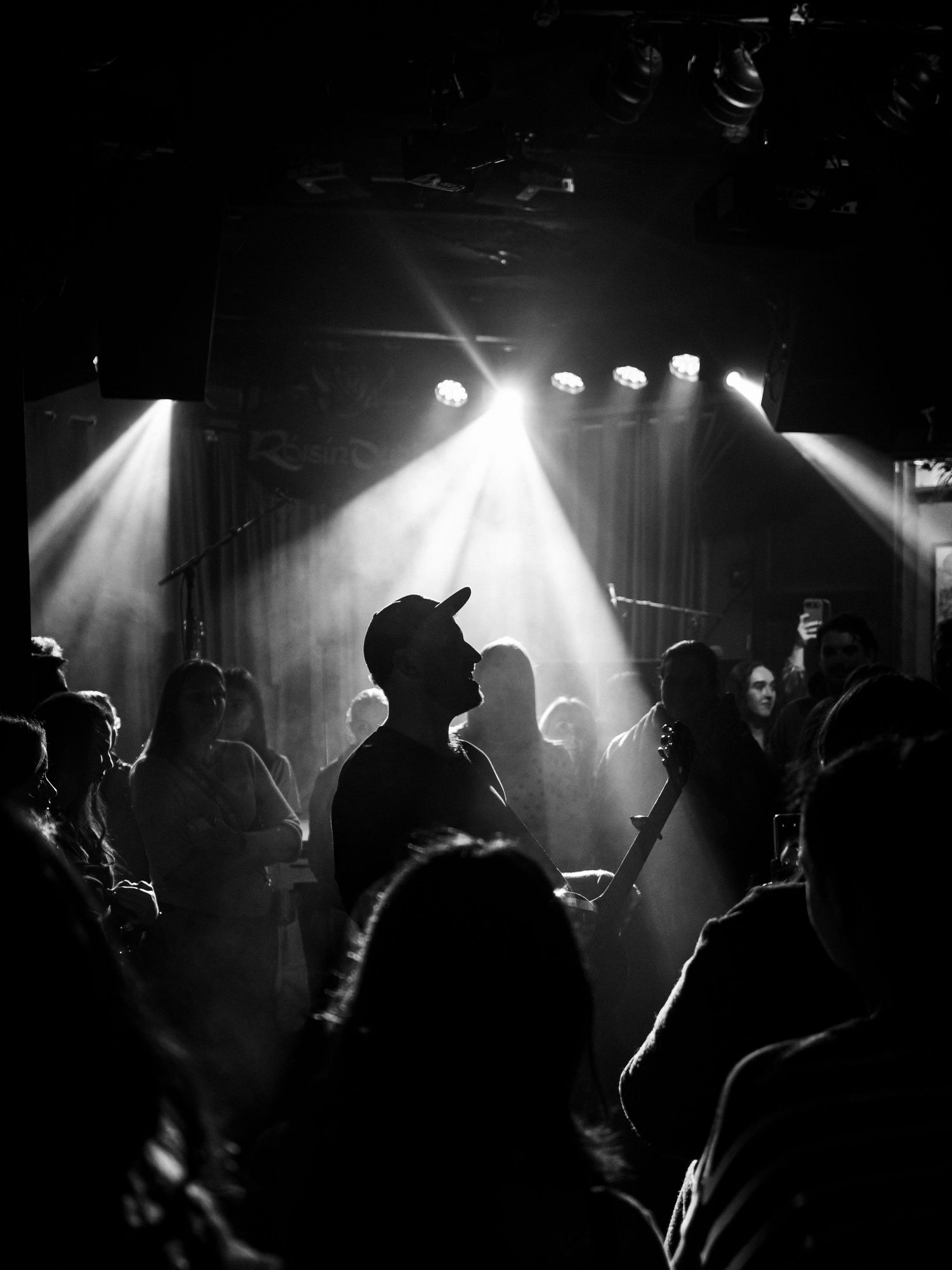 Silhouettes of concert crowd against dramatic stage lighting in black and white photography.