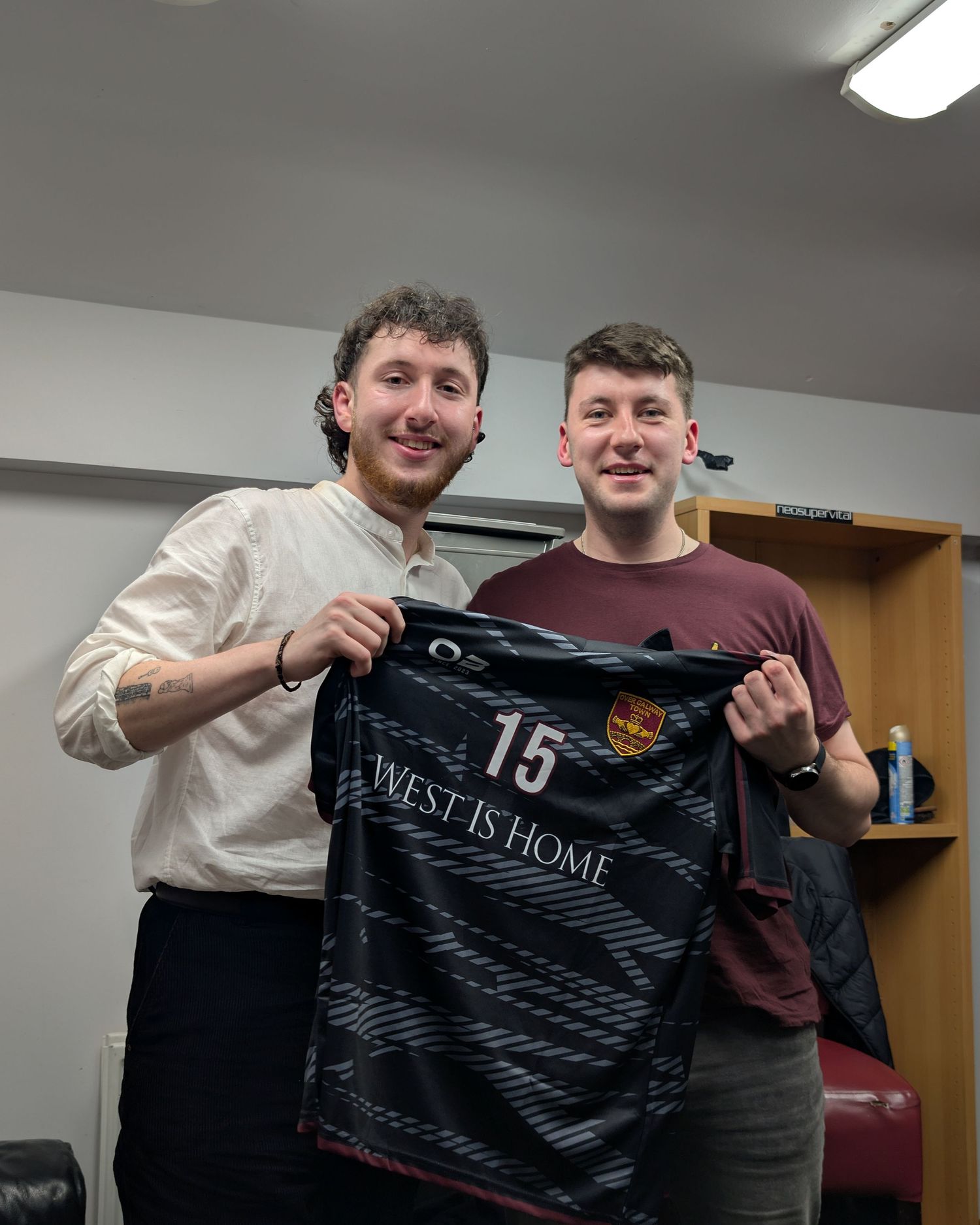 Two people in a locker room holding up a black soccer jersey with number 15 and 