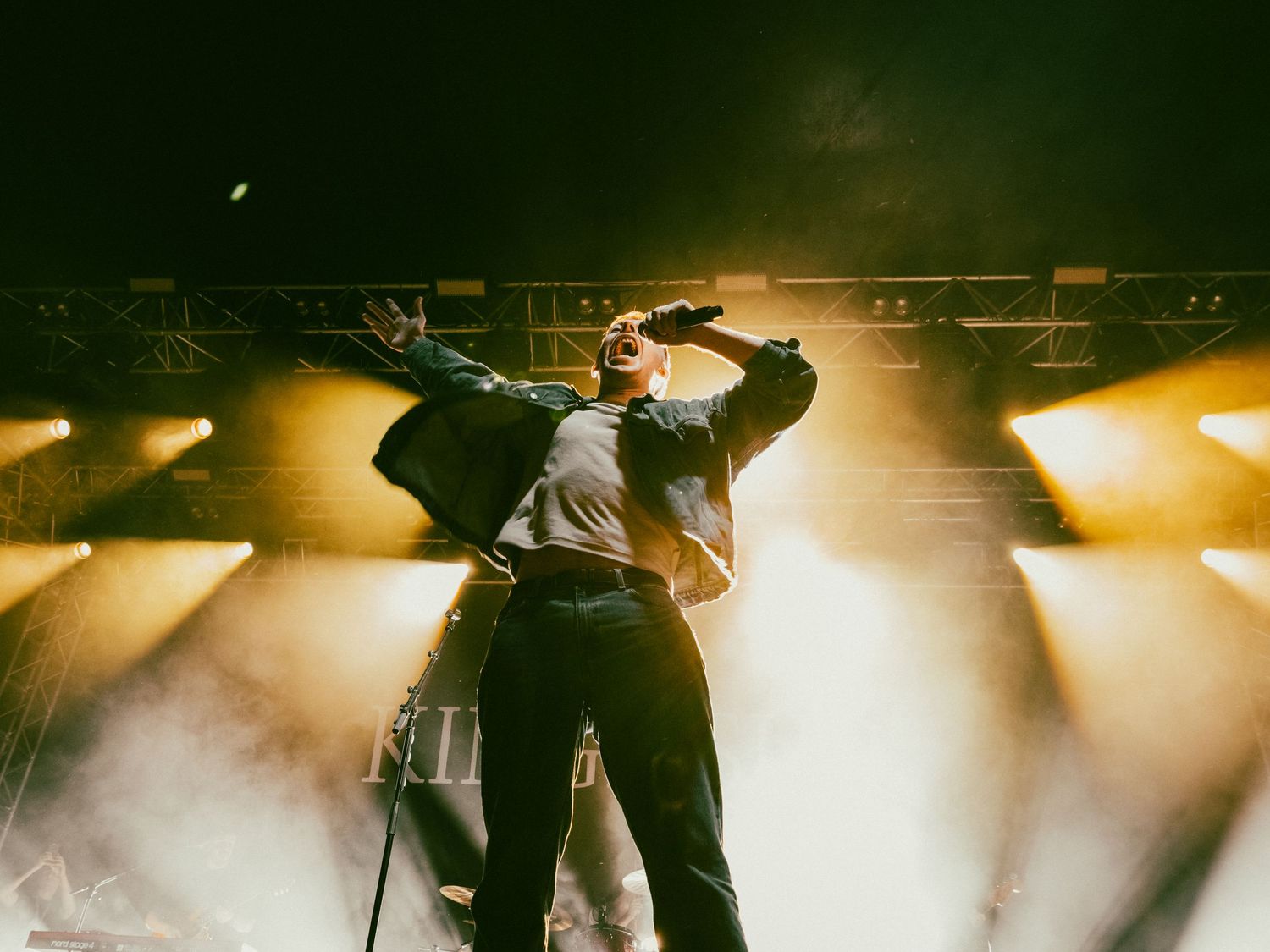 Dramatic concert scene with performer silhouetted against golden stage lights and fog effects.
