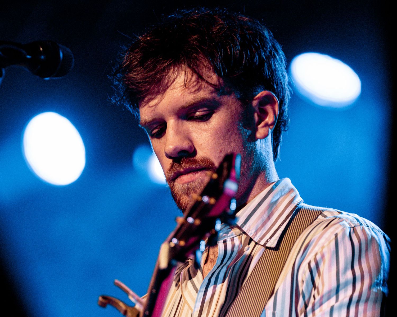 Musician performing on stage with blue lighting and striped shirt during live concert.