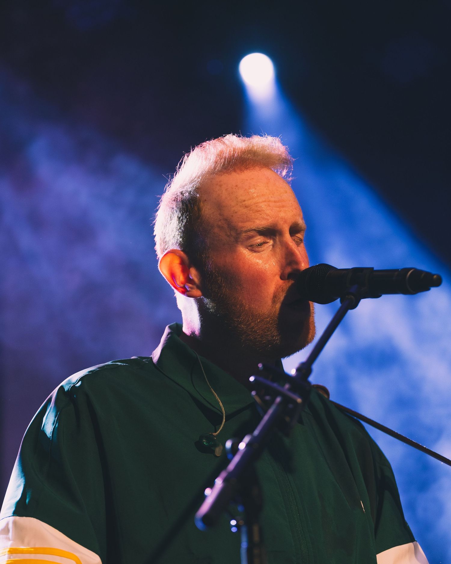 Dramatic side profile of a performer singing on stage with blue lighting and fog effects.