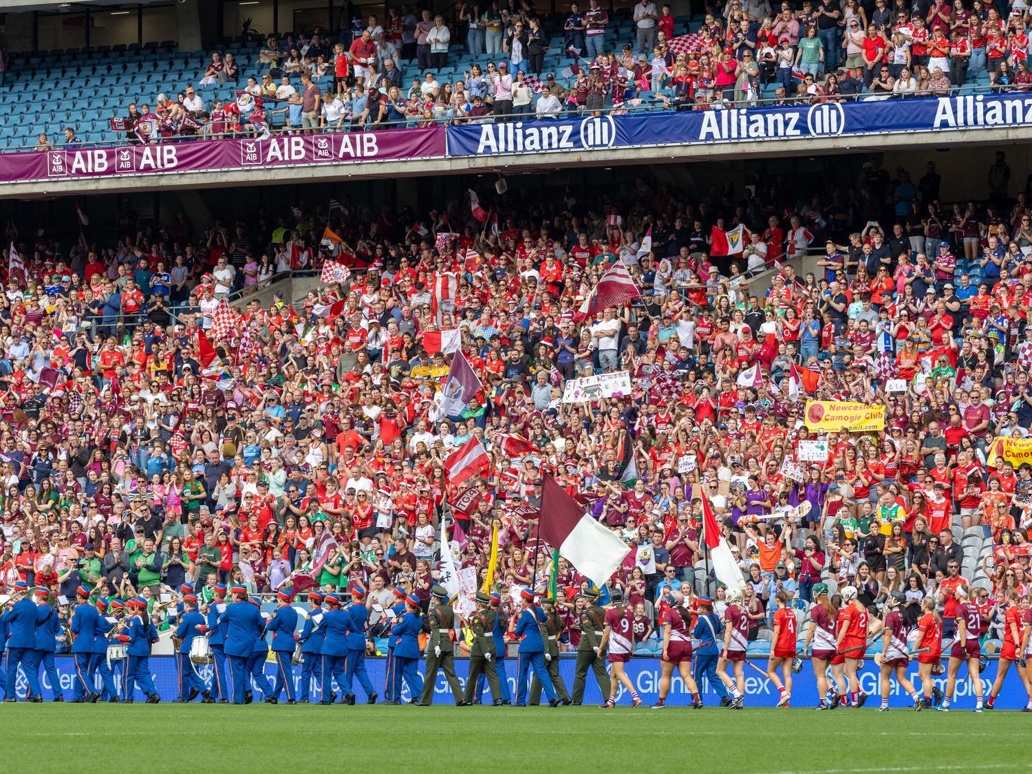 Packed stadium crowd with red-clad supporters watching a sporting event behind Allianz advertising boards.