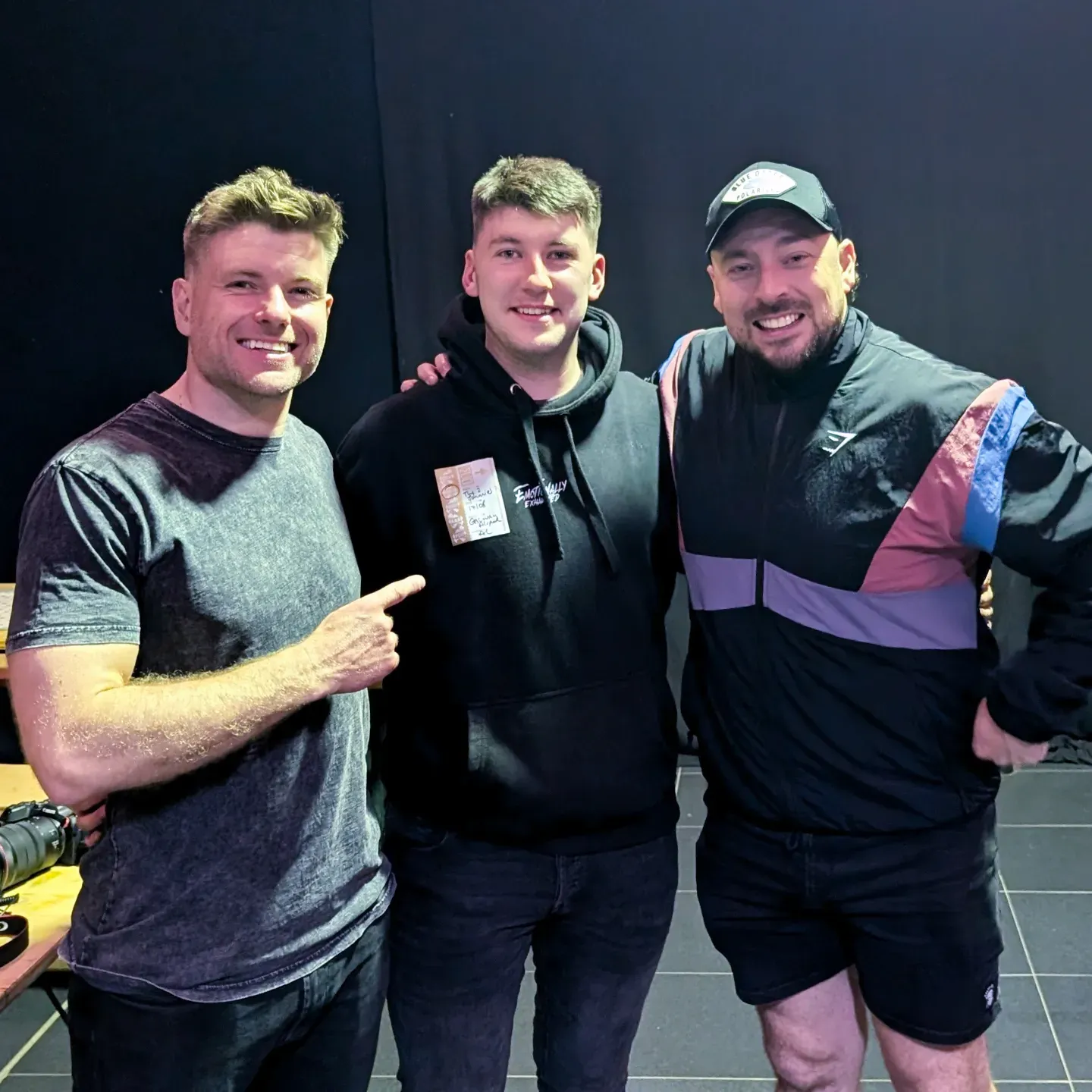 Three people wearing casual athletic wear pose together and smile in an indoor setting.