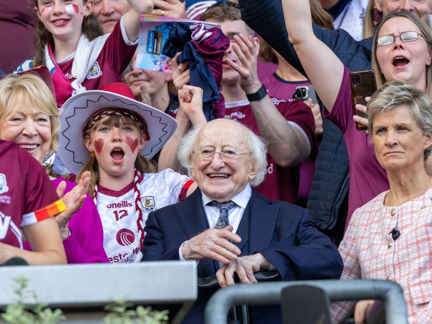 Enthusiastic fans in maroon attire cheer and celebrate during a sporting event.