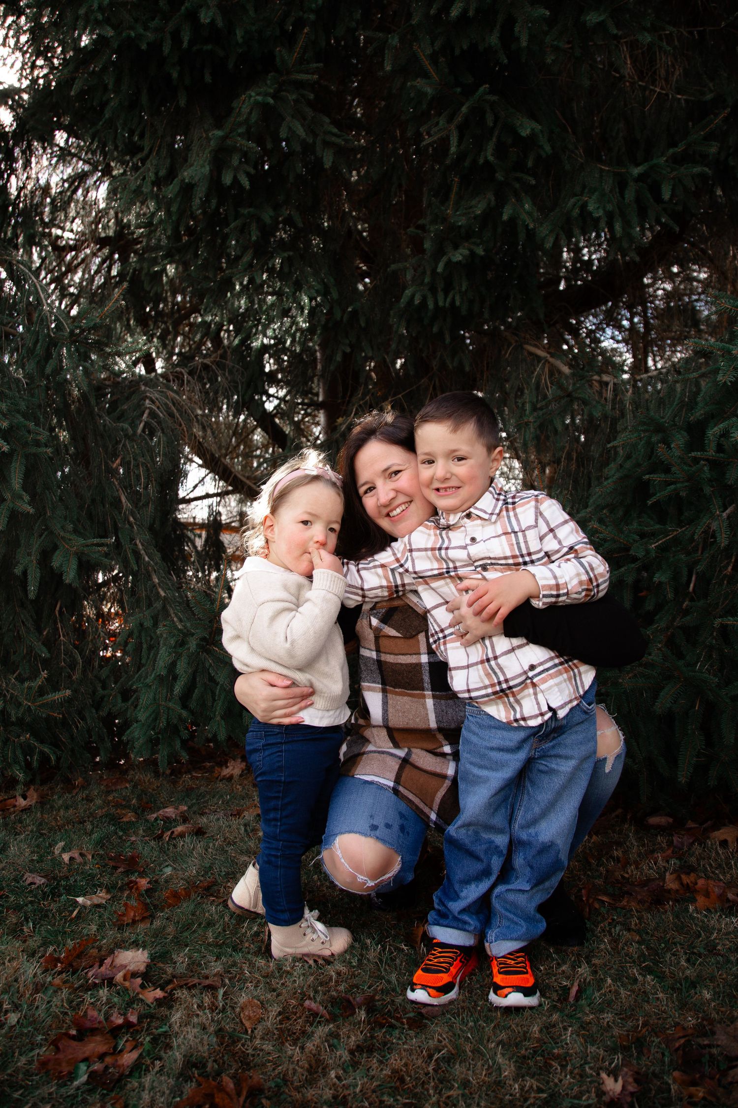 Two young children in casual outfits embrace while playing outdoors in front of greenery.