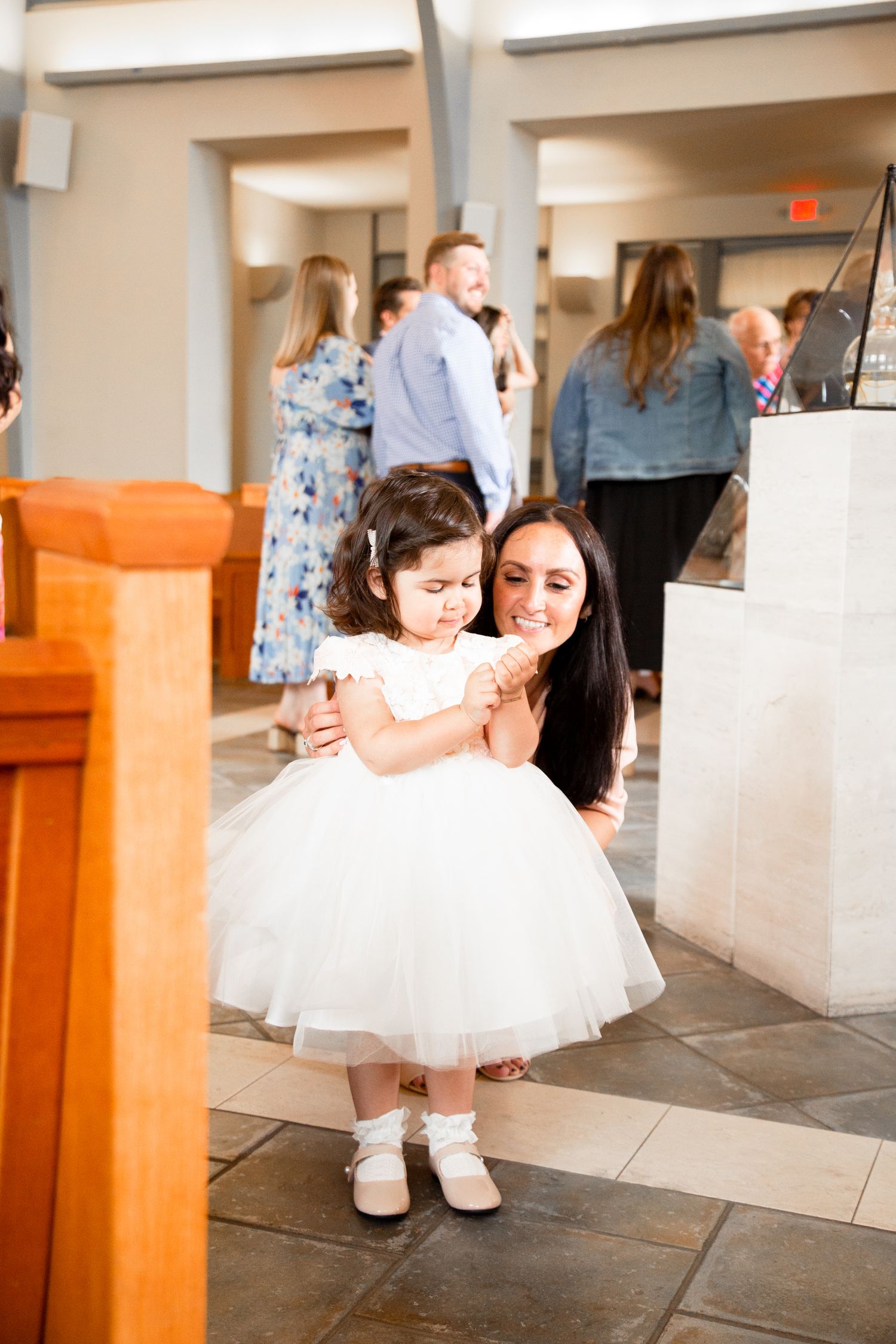 A child in a white tulle dress spins and twirls playfully around orange wooden pillars in a hallway.