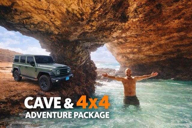 Cave and 4x4 adventure package in Aruba with a man posing in a rocky sea cave beside a green SUV.