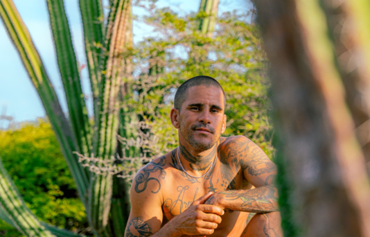 “Aruba portrait photoshoot with a tattooed man posing in natural cactus gardens at golden hour.”
