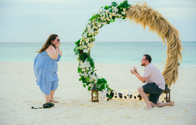 “Aruba surprise proposal photoshoot at the beach with a floral arch, captured by Aruba couples and engagement photographer Vince Camargo.”