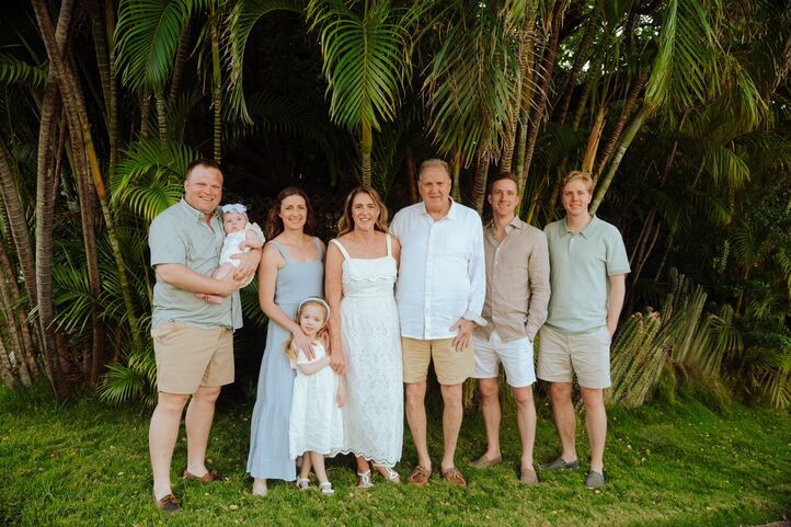 Family of seven posing together outdoors among lush tropical palm trees on a sunny day.